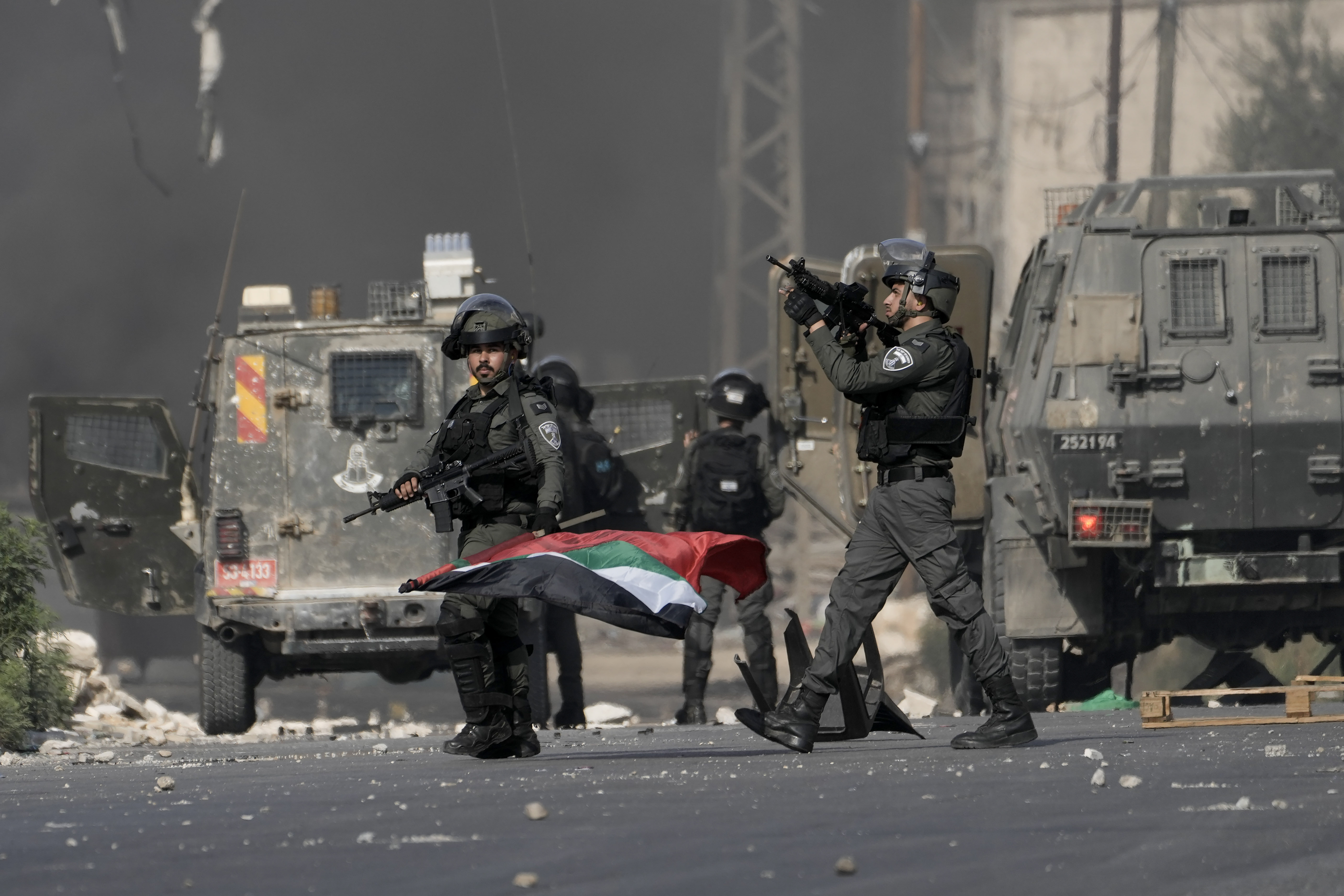 Israeli bored policeman holds a Palestinian flag he took from Palestinians during clashes following a demonstration in support of the Gaza Strip in the West Bank city of Nablus, Friday, Oct. 13, 2023.