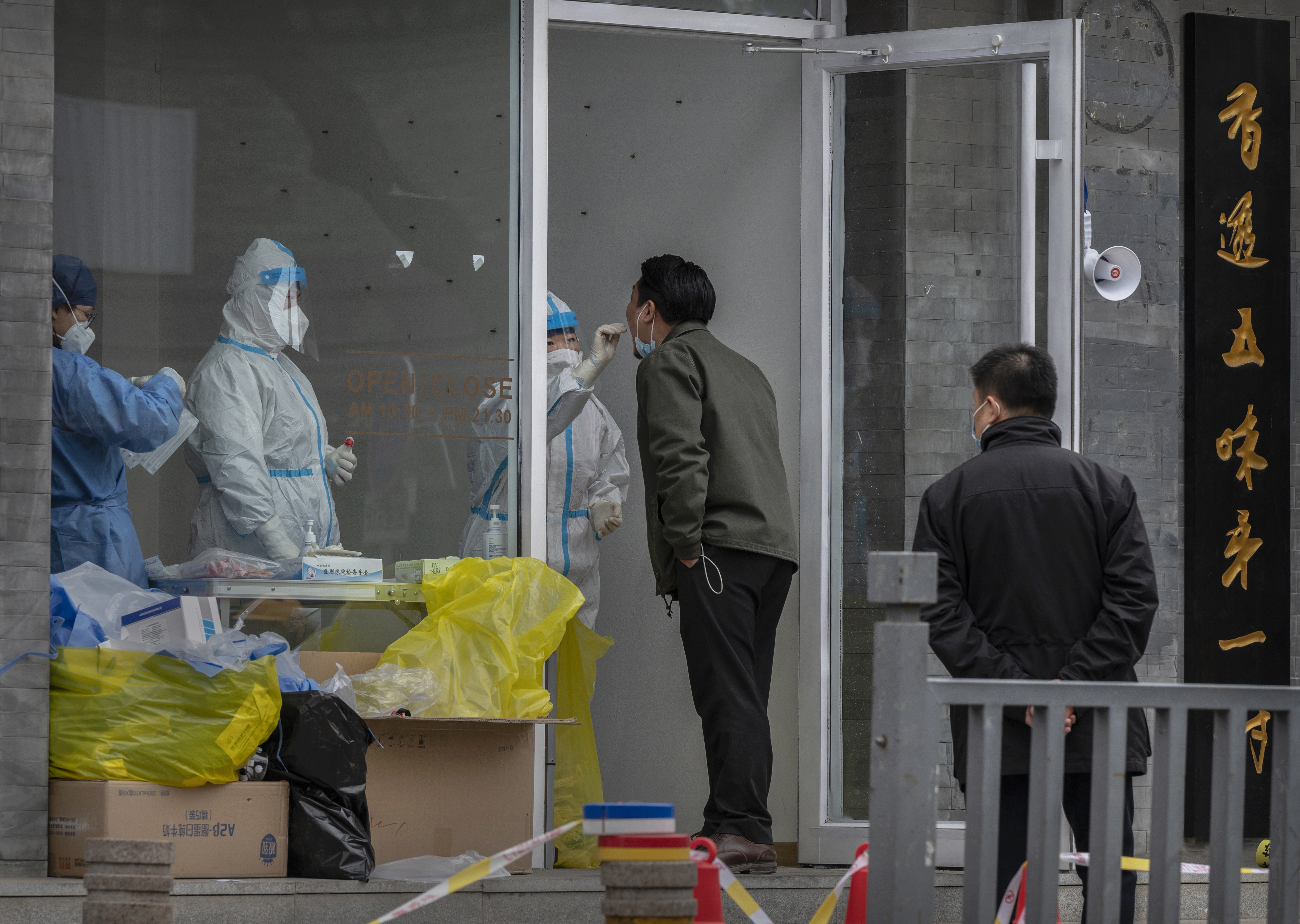 BEIJING, CHINA - MARCH 25: A health worker wears a protective suit as she performs a nucleic acid test to detect COVID-19 on a local resident at a pop-up testing site in the street on March 25, 2022 in Beijing, China. China has stepped up efforts to control a recent surge in coronavirus cases across the country, locking down the entire province of Jilin and the city of Shenyang and putting others like Shenzhen and Shanghai under restrictions. Local authorities across the country are mass testing