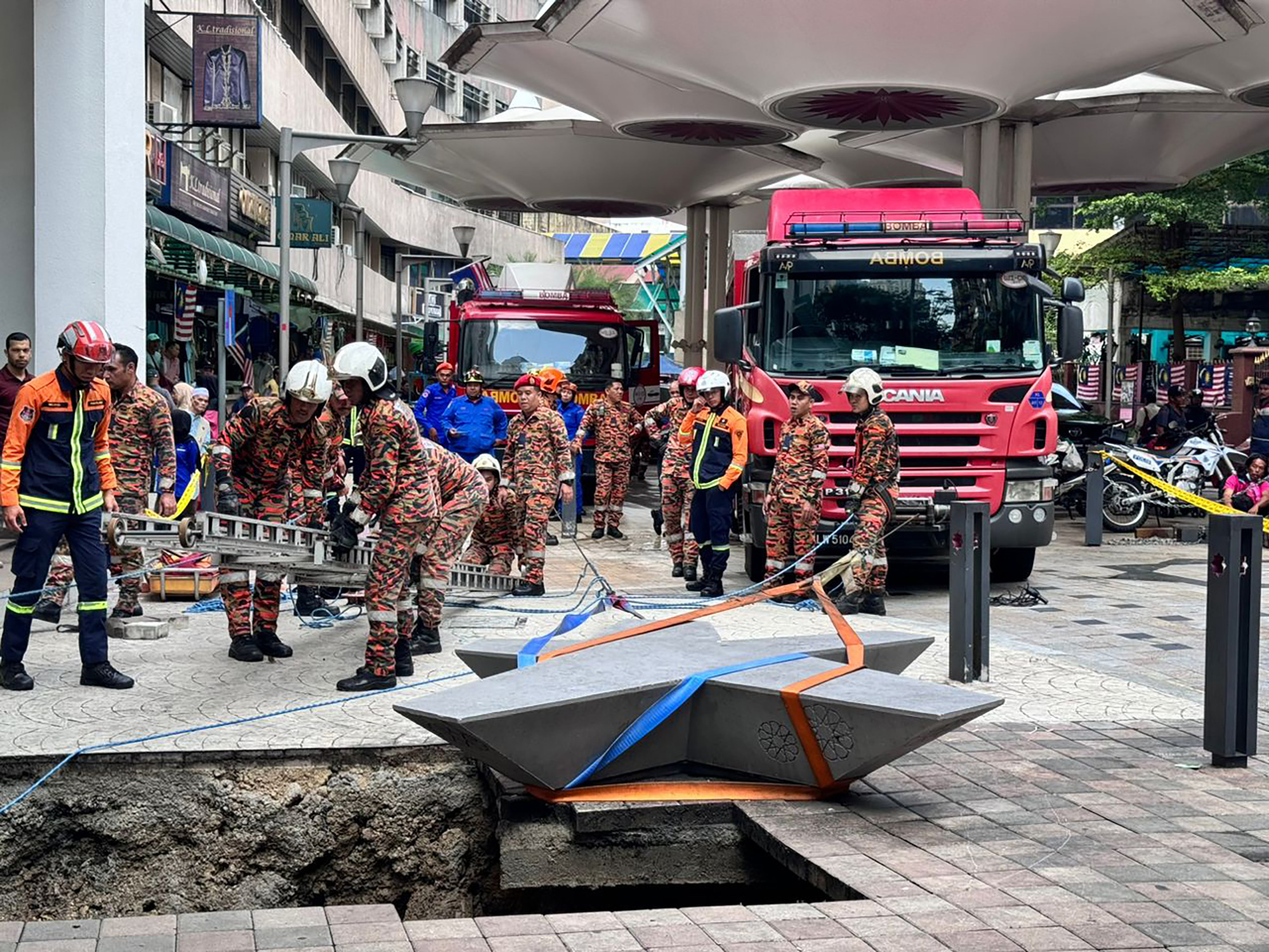 This photograph provided by Fire and Rescue Department of Malaysia, shows rescue personnel entering a deep sinkhole after receiving reports that a woman has fallen into the sinkhole after a section of the sidewalk caved in Kuala Lumpur, Friday, Aug. 23, 2024 