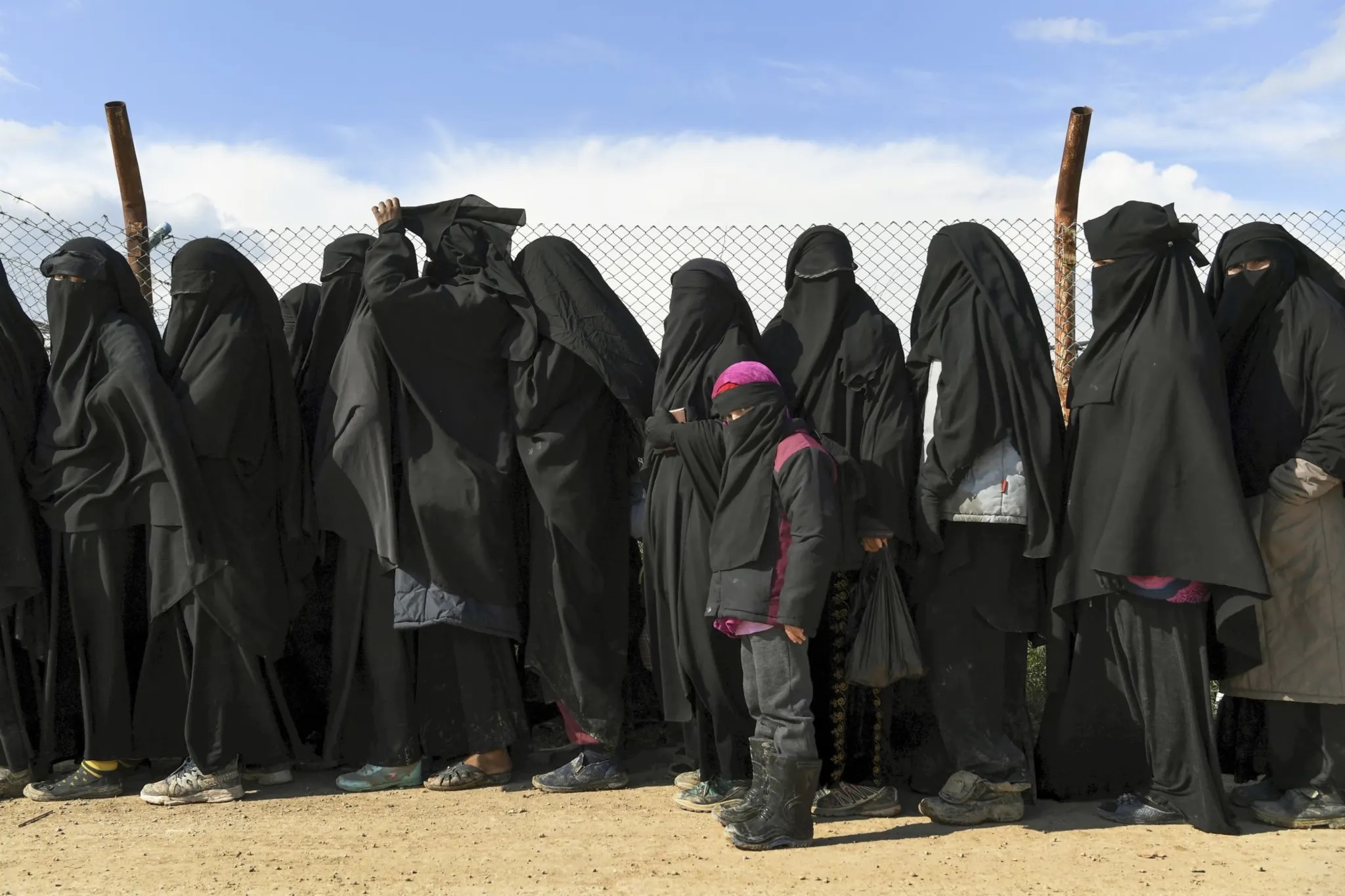 Esposas e hijos extranjeros del Estado Islámico hacen fila en un campamento en Siria para ser llevados a las tiendas en 2019.