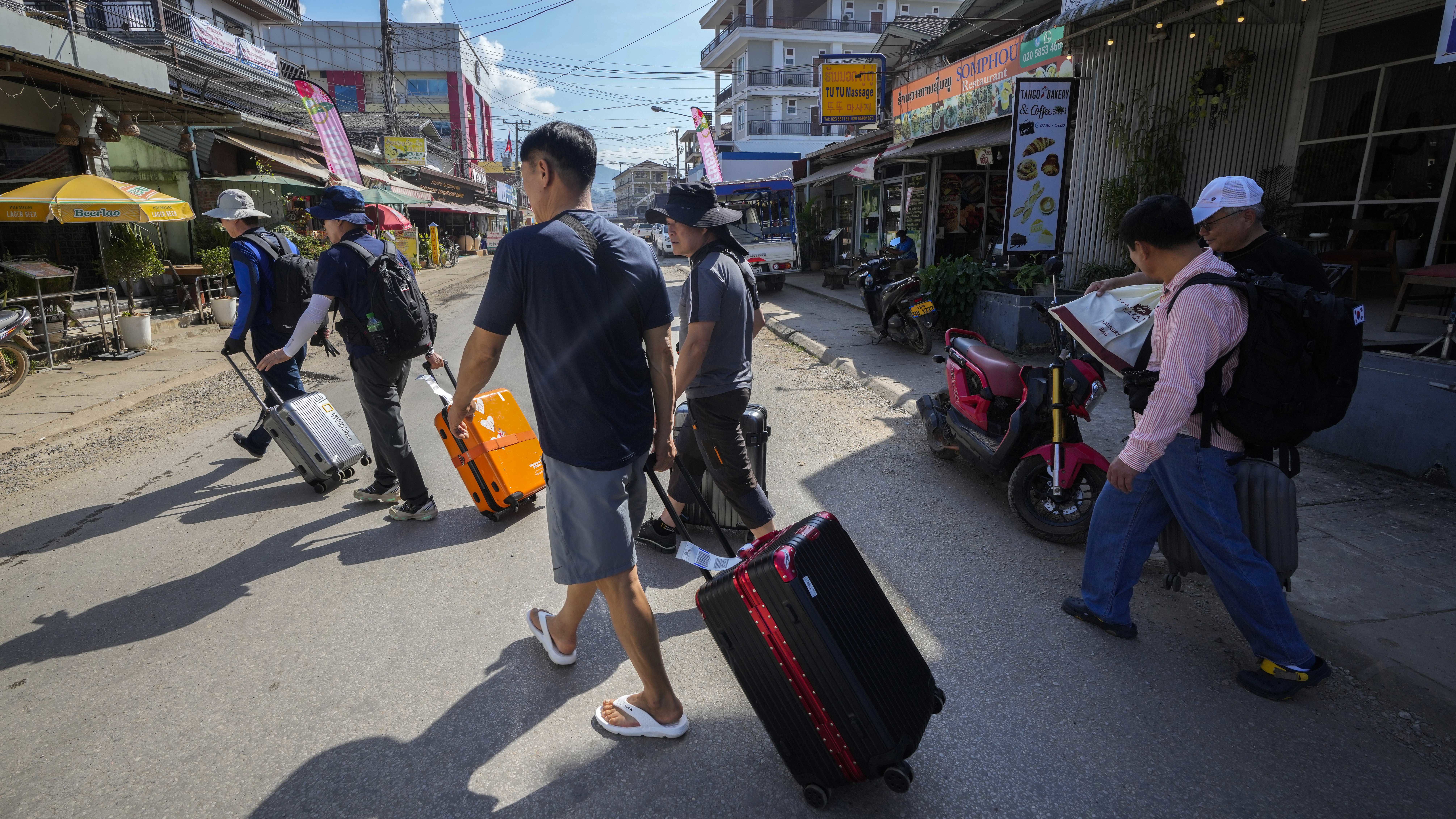 A group of travellers cross a road with their luggage in Vang Vieng, Laos.