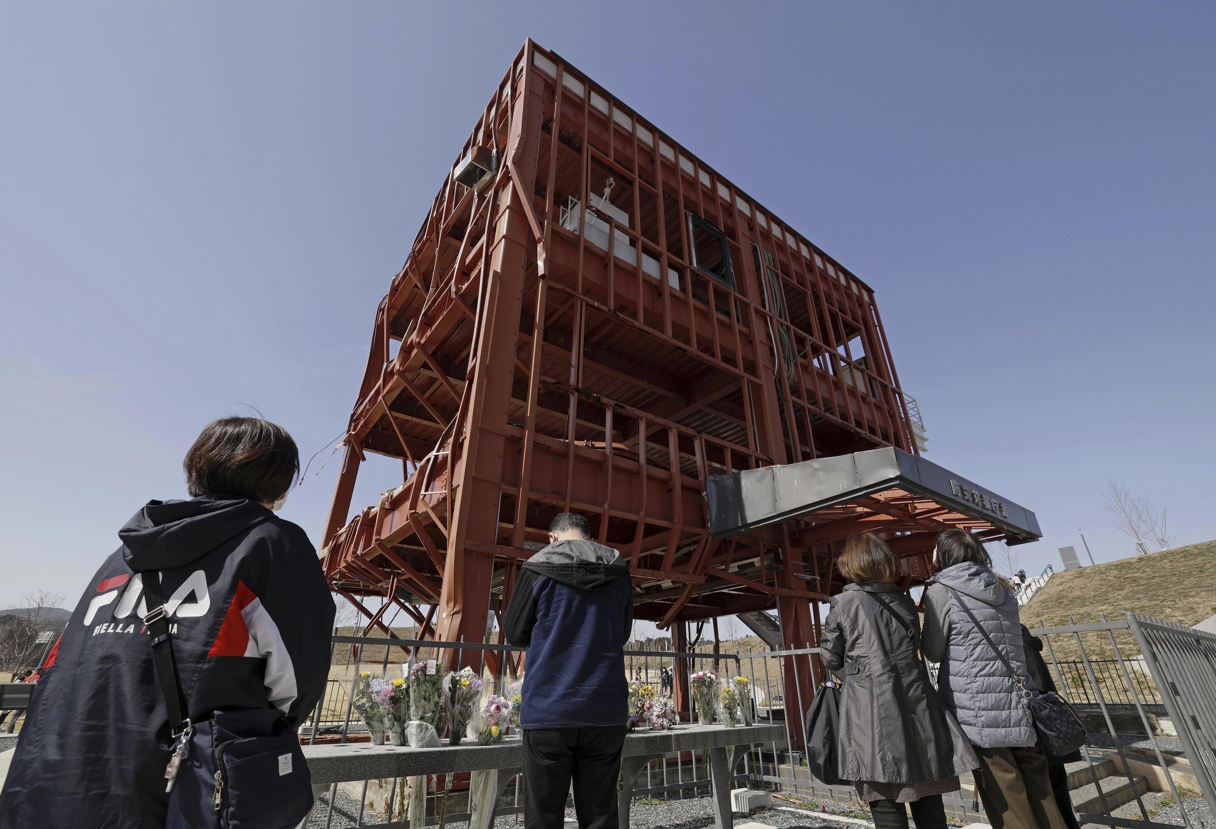 People offer prayers at the skeleton of the tsunami-damaged disaster prevention headquarters where dozens of workers died in the 2011 tsunami in Minamisanriku, Miyagi Prefecture, northern Japan, Saturday, March 11, 2023. 