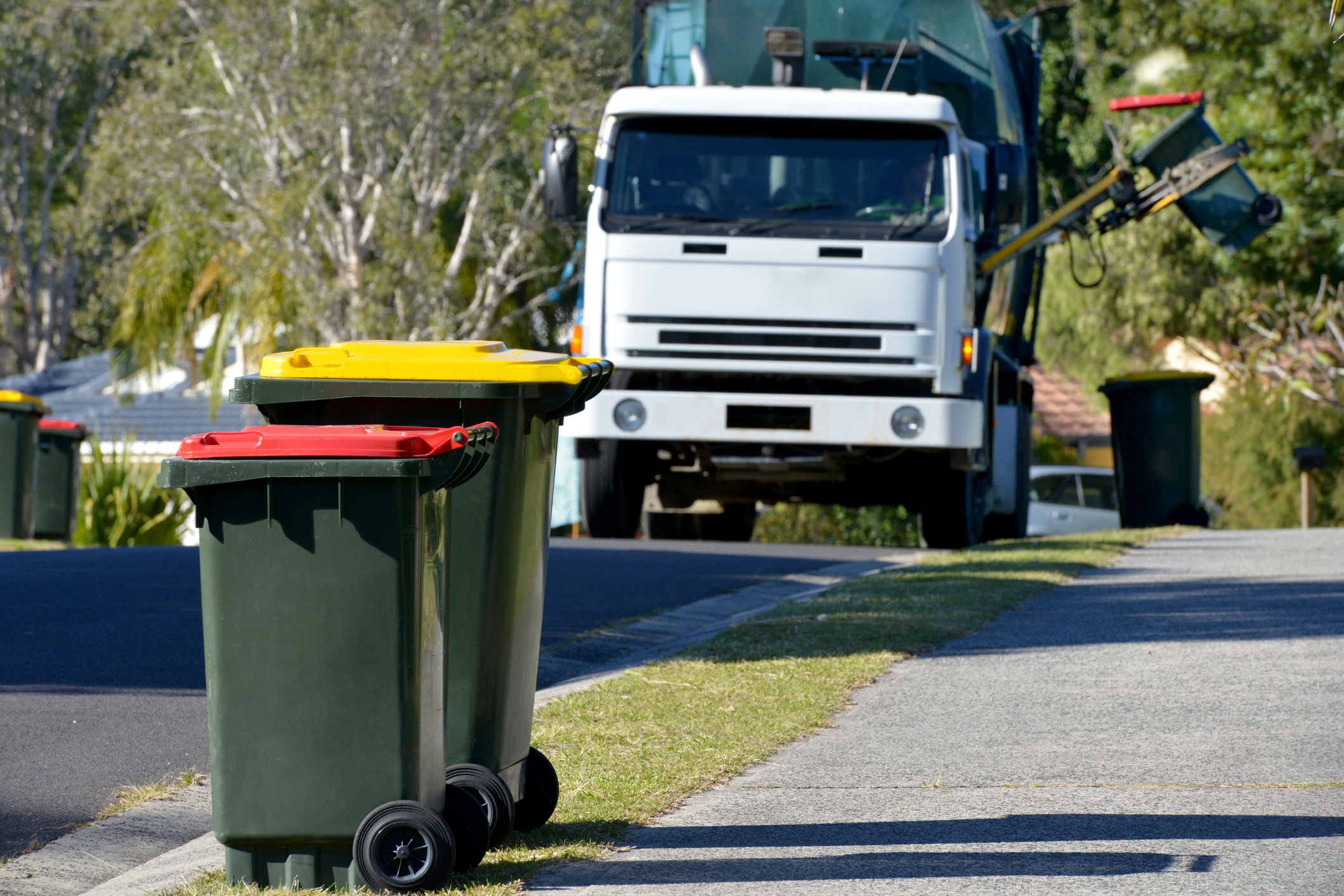 Focus on two Rubbish bins with rubbish truck in background lifting a bin