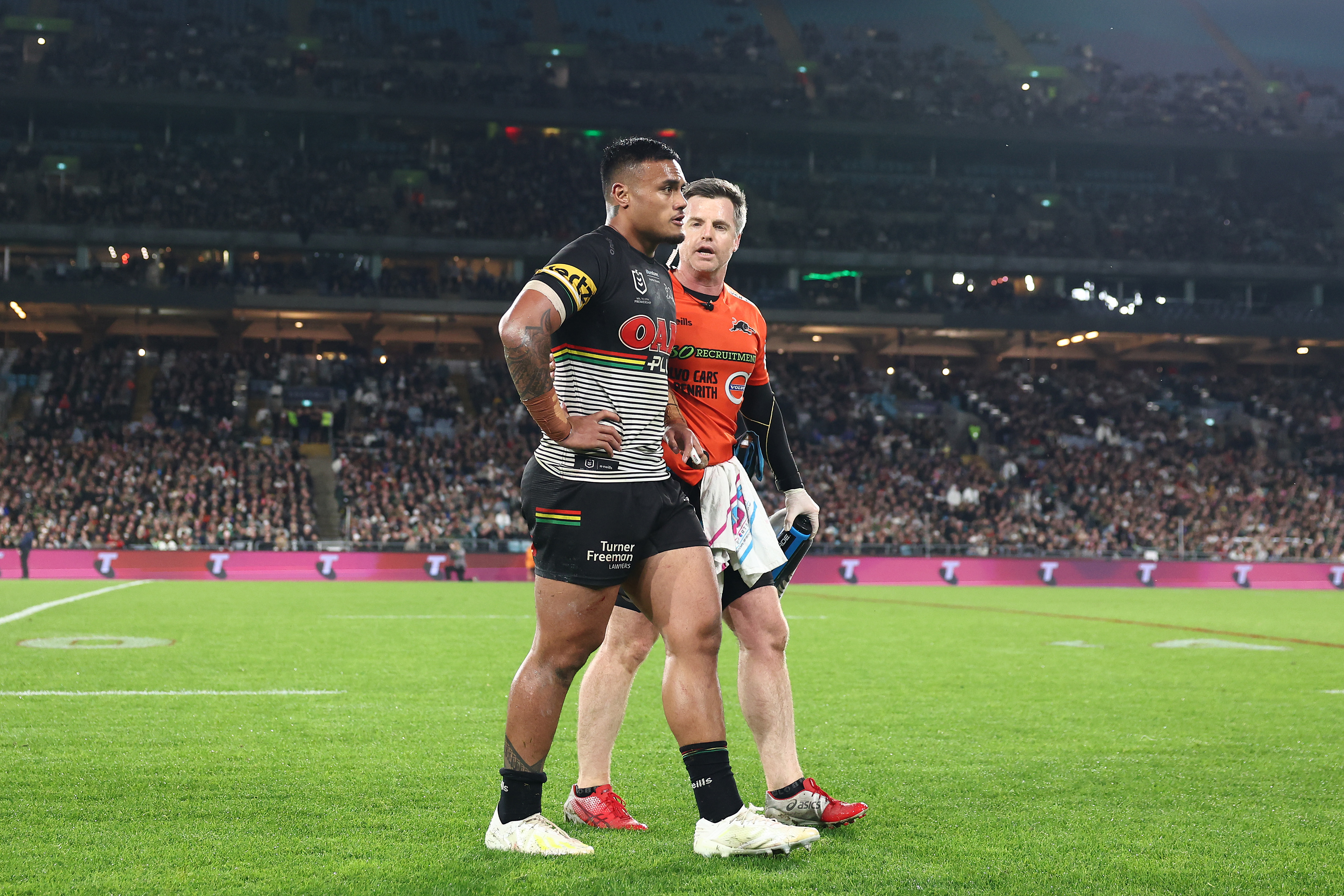 Penrith player Spencer Leniu is helped off the field by trainer Pete Green.