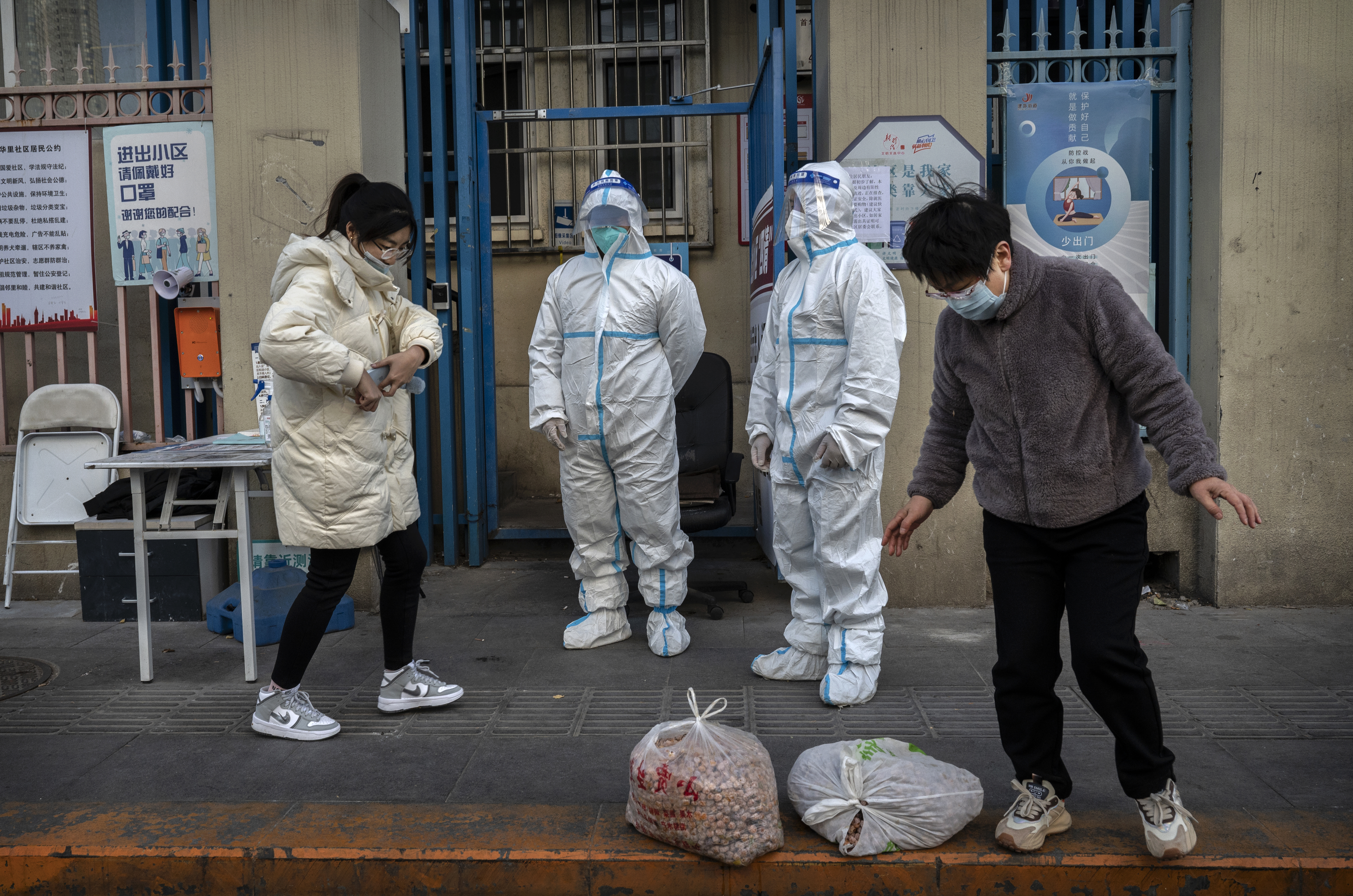 An epidemic control worker and a security guard wear protective suits to prevent the spread of COVID-19 as a resident collects a food order outside an apartment building in the Central Business District on November 26, 2022 in Beijing, China. 