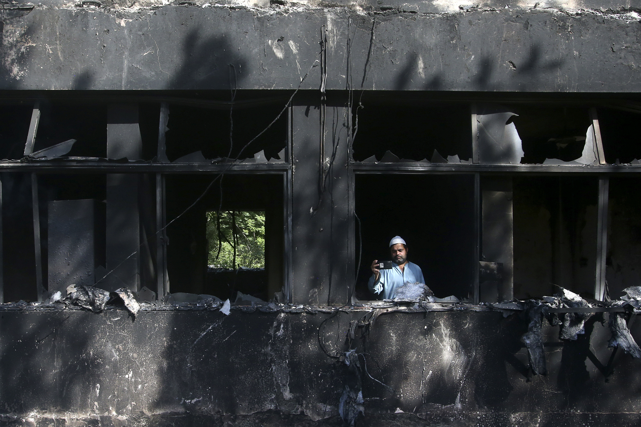 A man takes a photo with his mobile phone inside the Radio Pakistan building burnt in Wednesday's clashes between police and the supporters of Pakistan's former Prime Minister Imran Khan, in Peshawar, Pakistan, Thursday, May 11, 2023. 