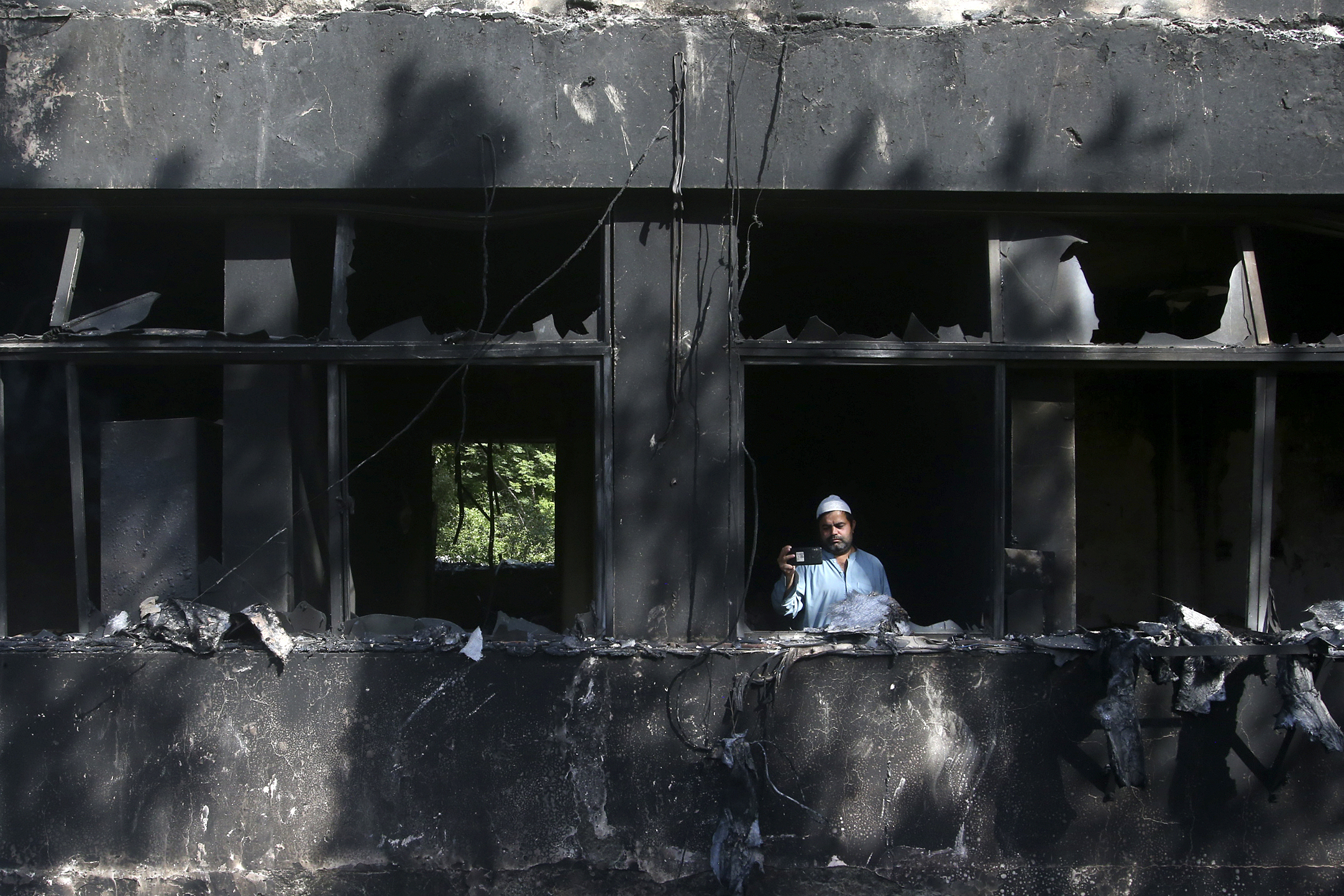 A man takes a photo with his mobile phone inside the Radio Pakistan building burnt in Wednesday's clashes between police and the supporters of Pakistan's former Prime Minister Imran Khan, in Peshawar, Pakistan, Thursday, May 11, 2023.