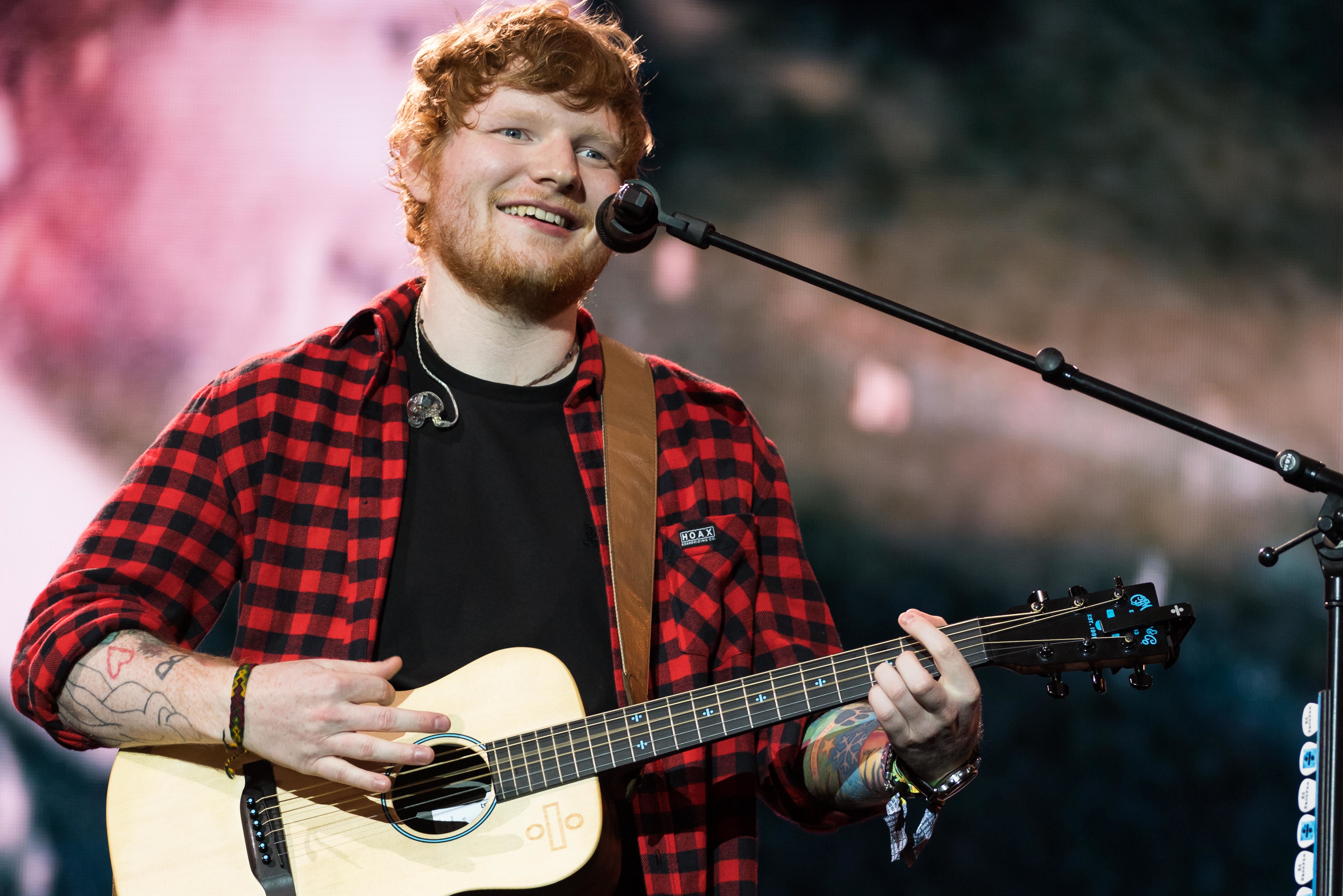 Ed Sheeran tocando la guitarra con micrófono en concierto 