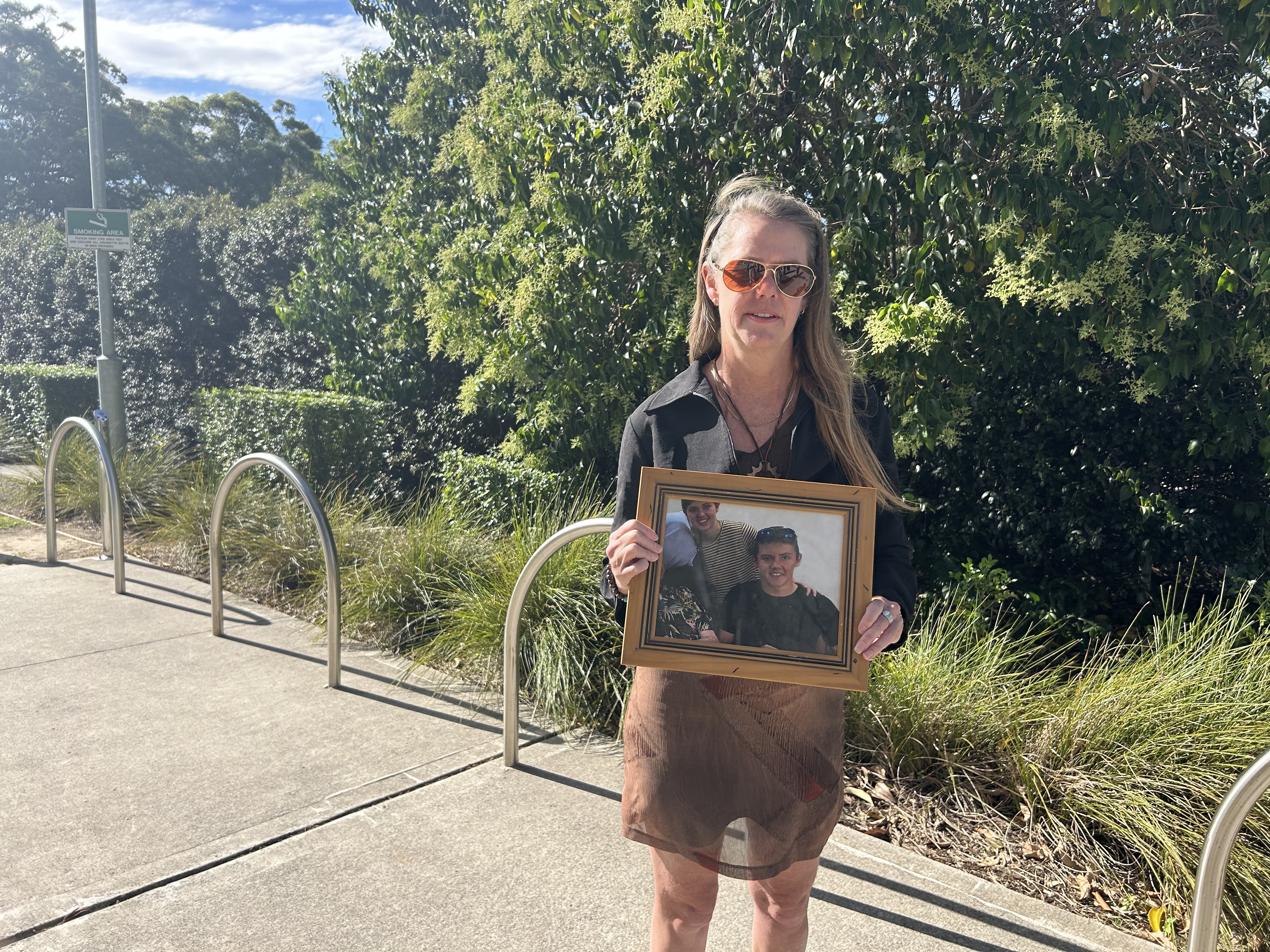 Myfanwy Webb holds a photo of her son Jeremy outside of Lidcombe Coroner's Court on the first day of the inquest into his death on November 17, 2025.