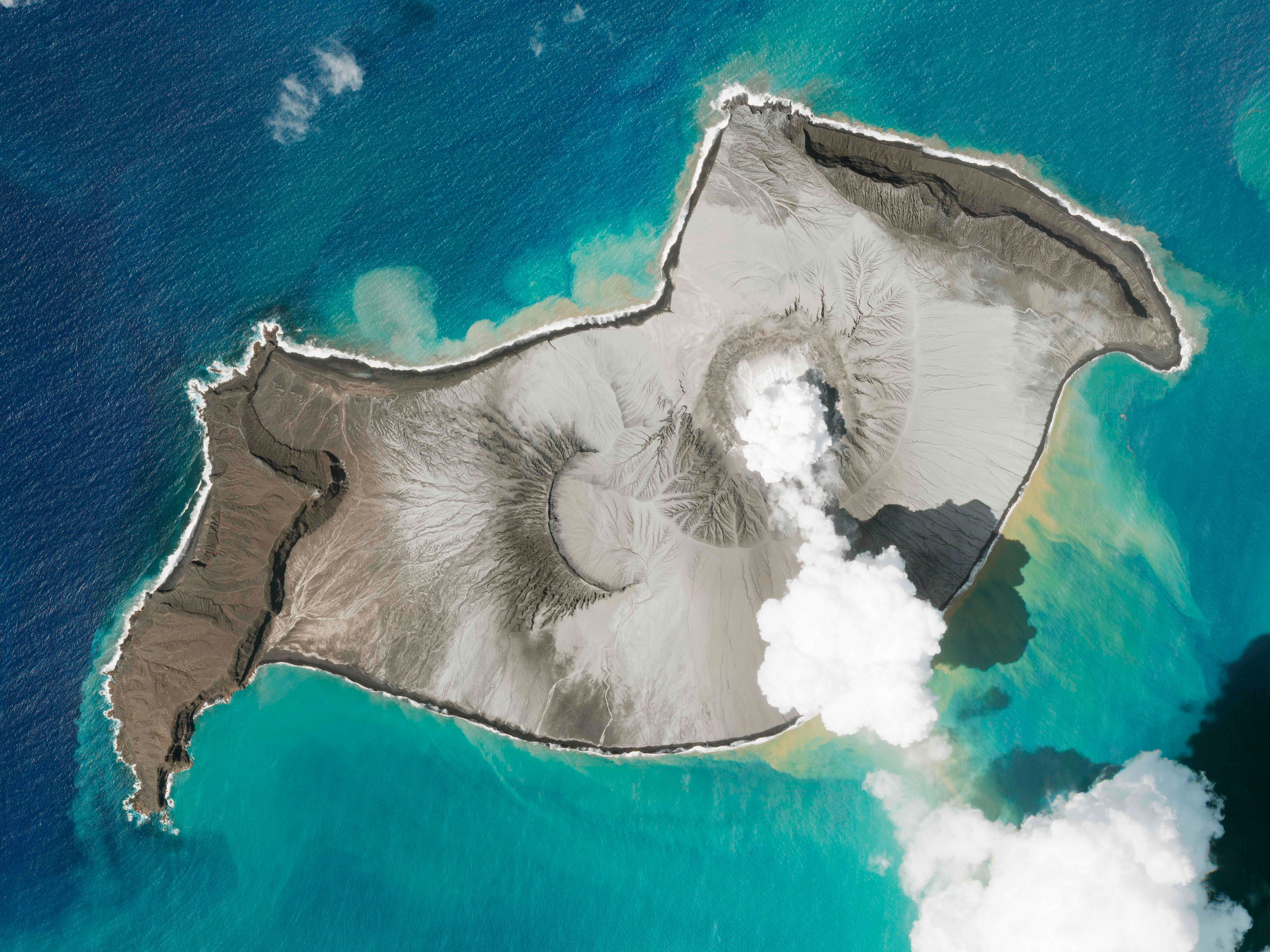 In this satellite photo taken by Planet Labs PBC, an island created by the underwater Hunga Tonga Hunga Ha'apai volcano is seen smoking on January 7. An undersea volcano erupted near Tonga yesterday, sending large tsunami waves crashing across the shore and people rushing to higher ground.