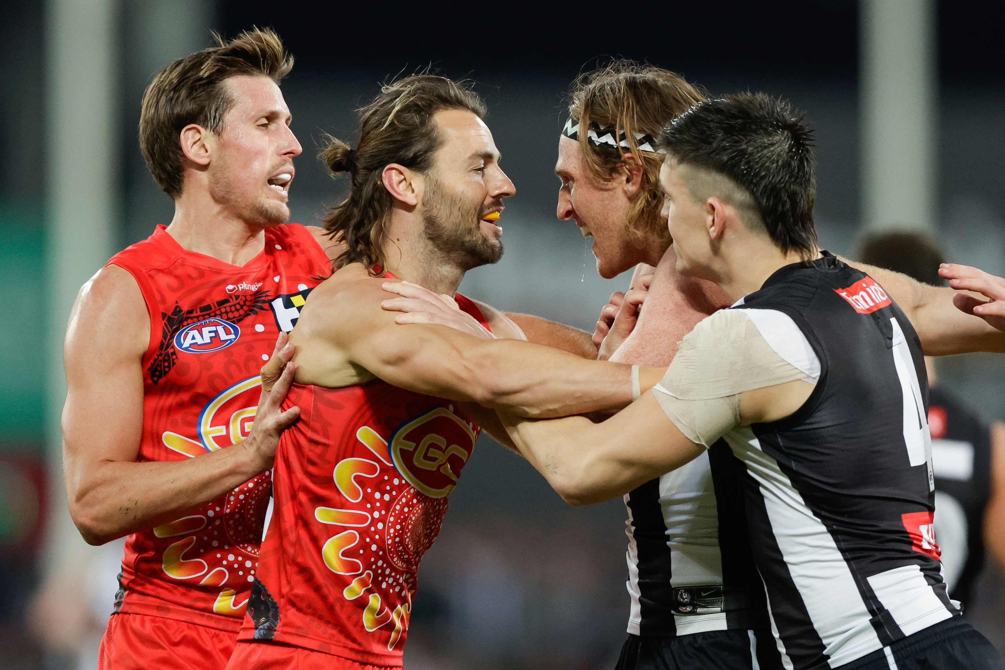 Lachie Weller of the Suns exchanges words with Nathan Murphy and Brayden Maynard of the Magpies.