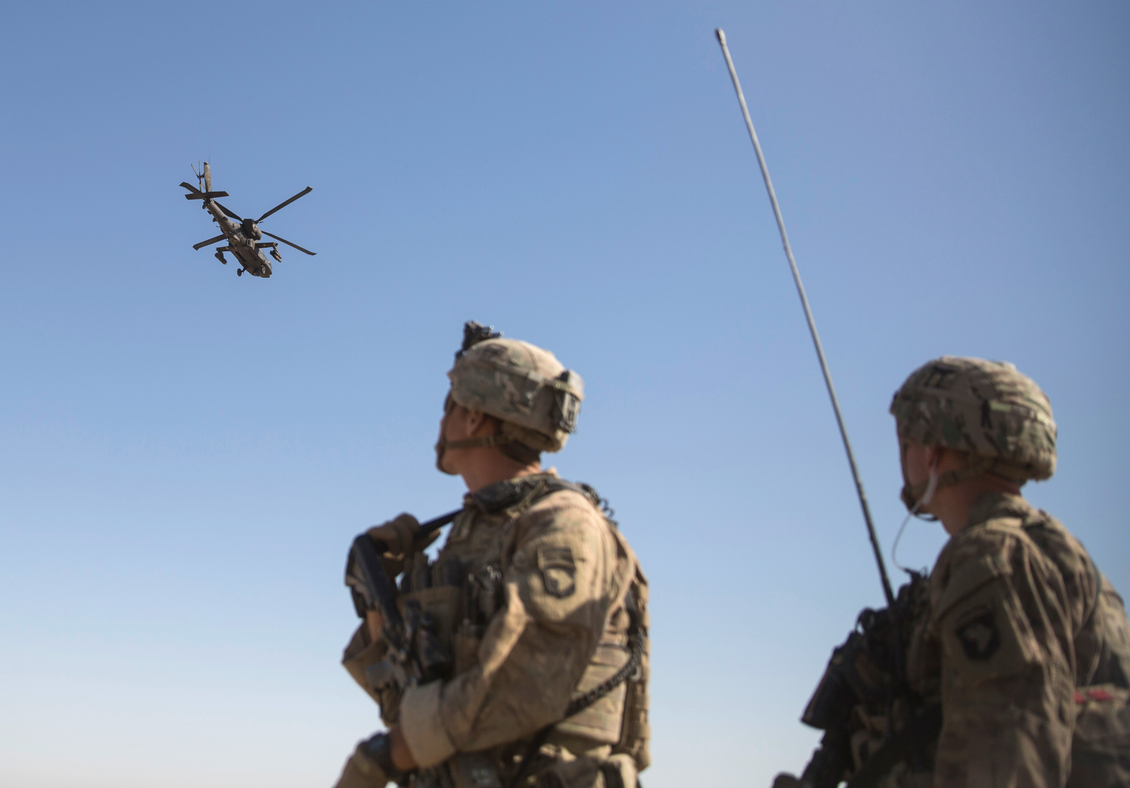 An AH-64 Apache attack helicopter flies above as US Soldiers at Task Force Iron at Bost Airfield in Afghanistan watch on.