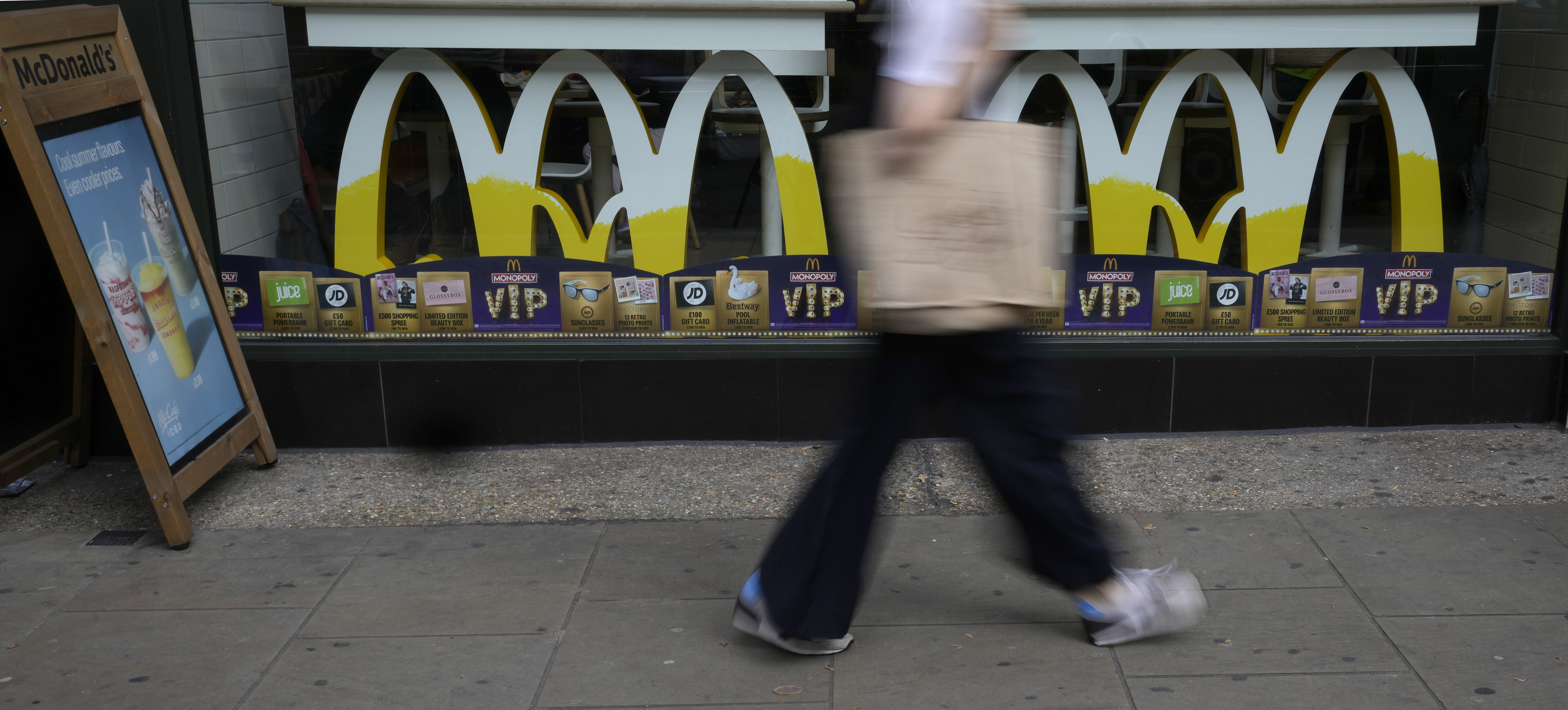 A woman walks by a McDonald's restaurant, in London, Tuesday, Aug. 24, 2021. McDonalds says it has pulled milkshakes from the menu in all 1,250 of its British restaurants because of supply problems stemming from a shortage of truck drivers. The fast-food chain says it is also experiencing shortages of bottled drinks. (AP Photo/Alastair Grant)