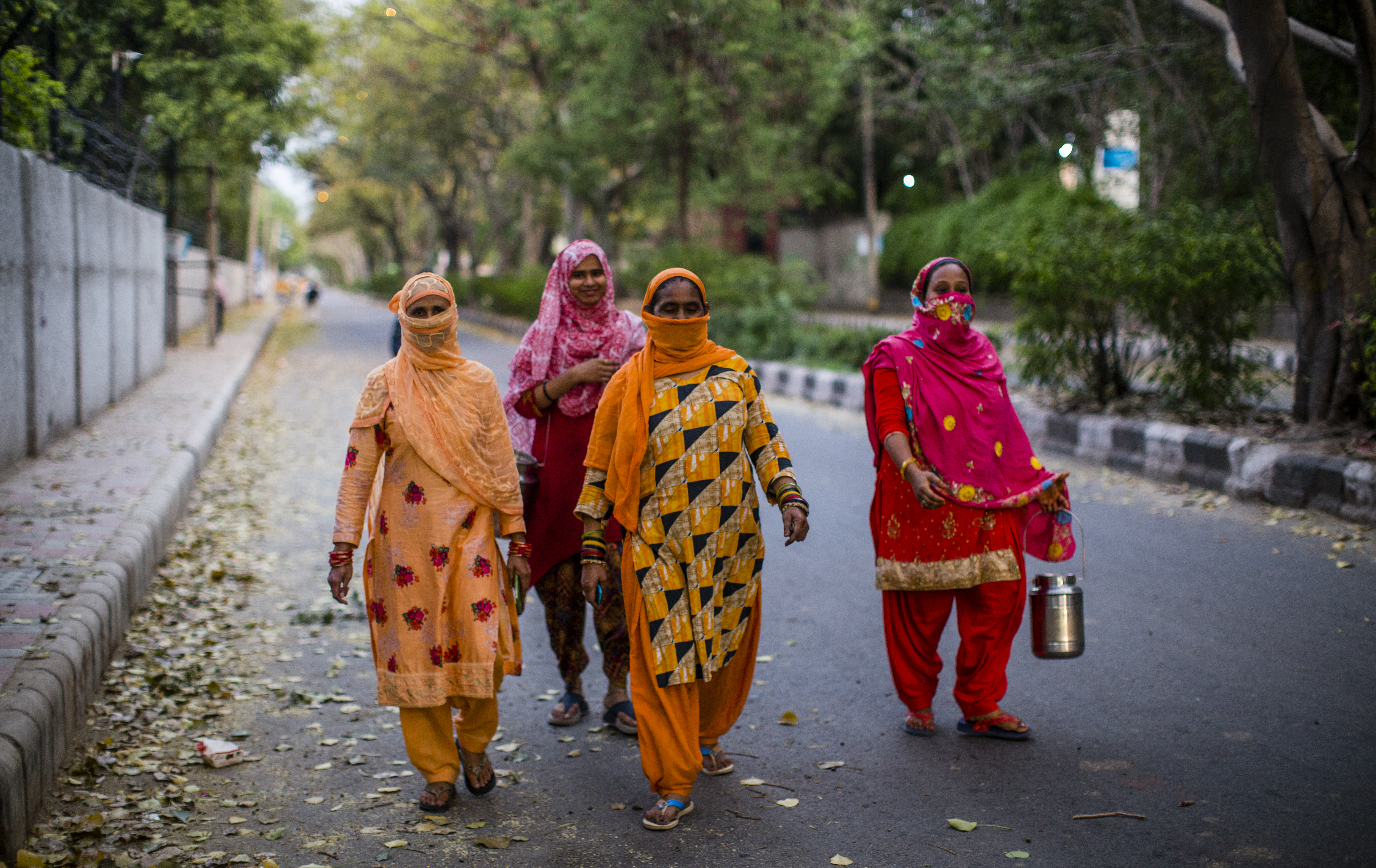 Indian women carry containers to buy milk as they walk on a deserted road , amid a nationwide lockdown.