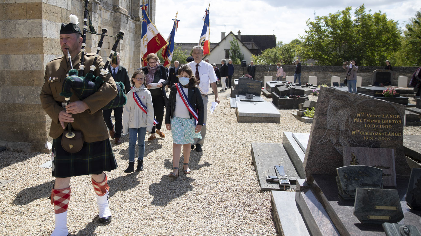 British expatriate Steven Oldrid, right, is led by a bagpiper as he directs a D-Day ceremony of laying flowers and wooden crosses for WWII dead at the local war cemetery in Benouville, Normandy, France on Saturday, June 6, 2020