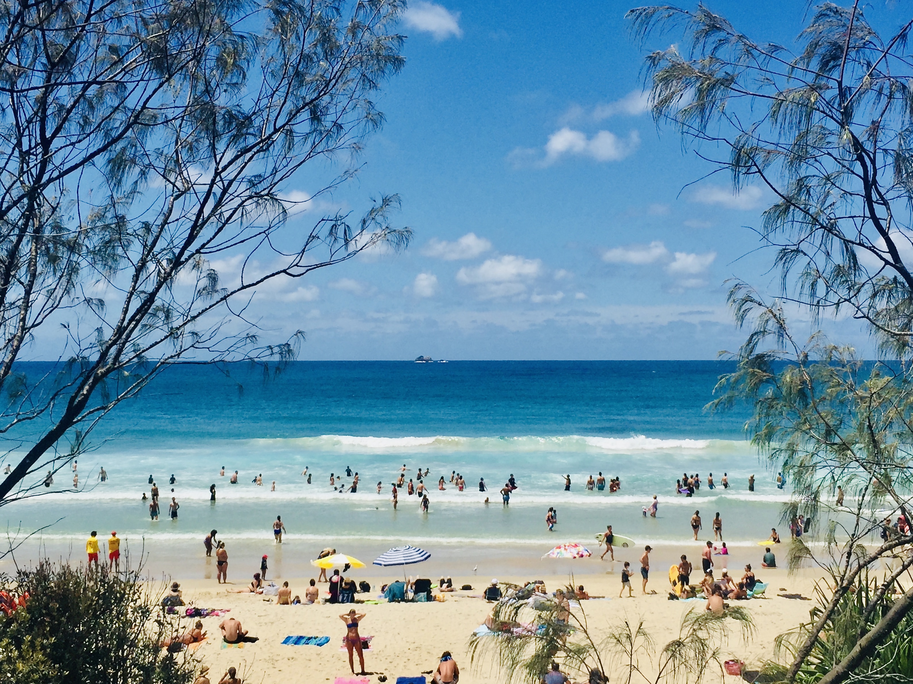 Horizontal Seascape of people enjoying the summer sun on busy tourist beach holiday with sand turquoise waves blue sky at famous surf ocean Byron Bay Australia