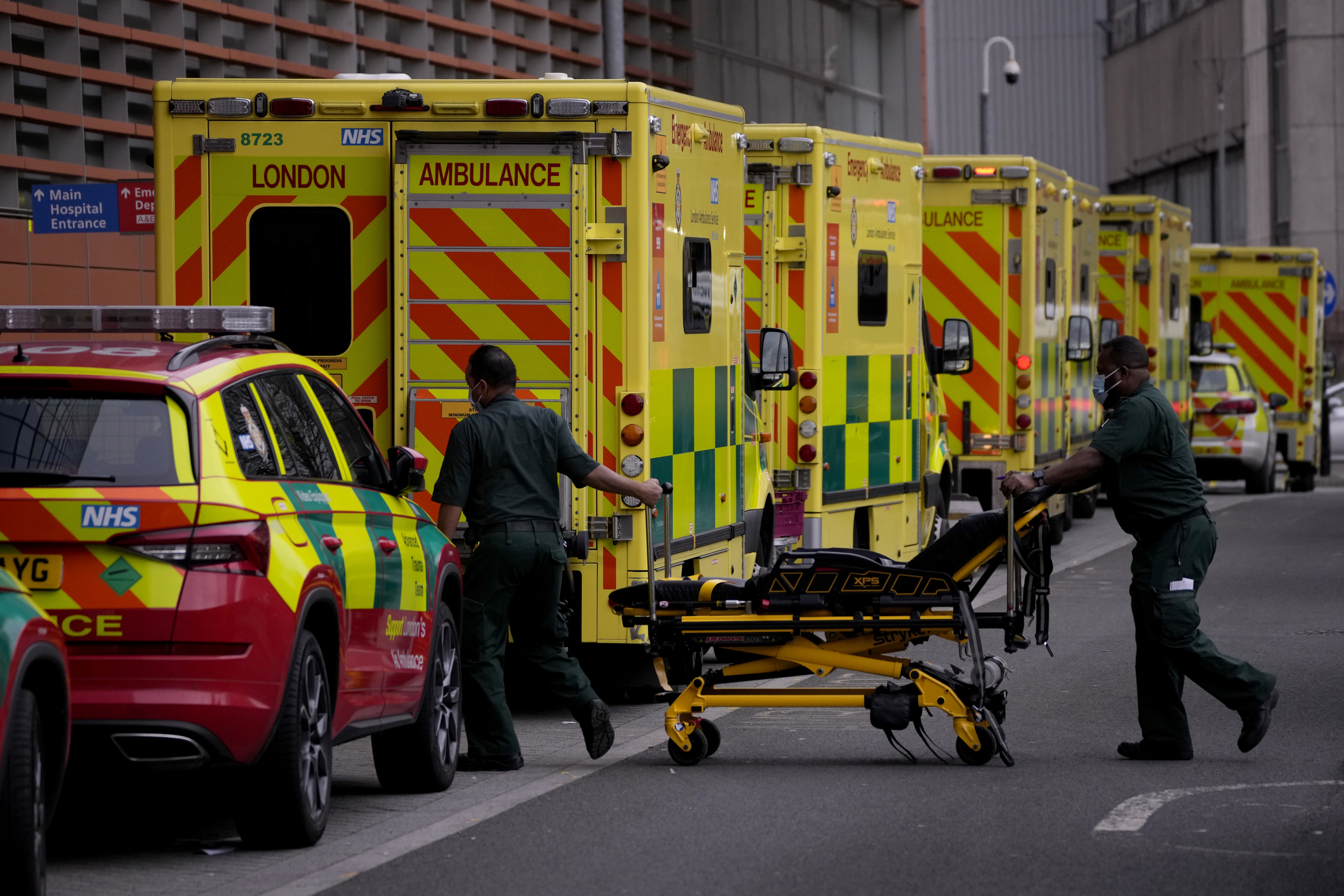 Paramedics push a trolley next to a line of ambulances outside the Royal London Hospital in the Whitechapel area of east London, Thursday, Jan. 6, 2022. 