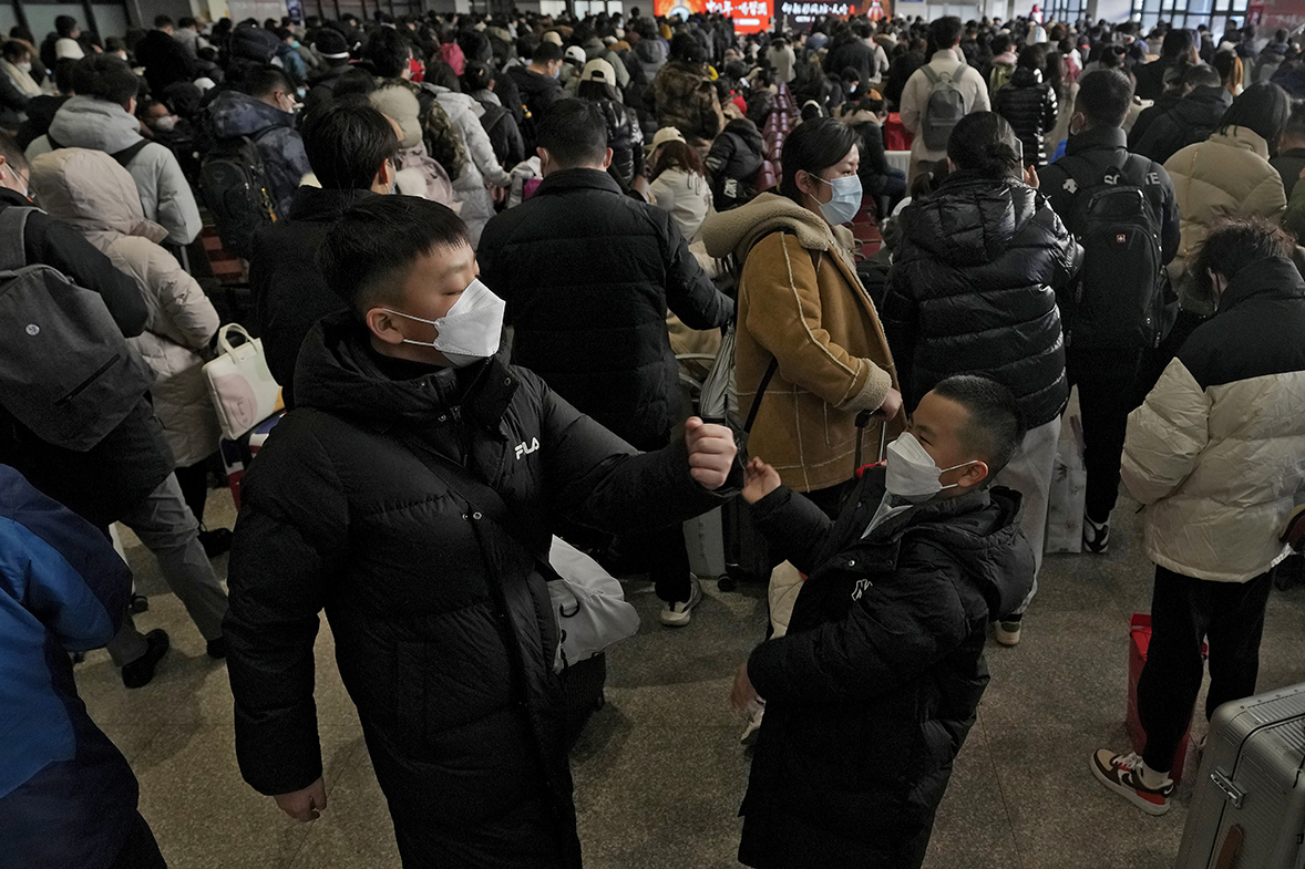 Children wearing face masks play each other as travelers with their luggage gather at a departure hall to catch their trains at the West Railway Station in Beijing