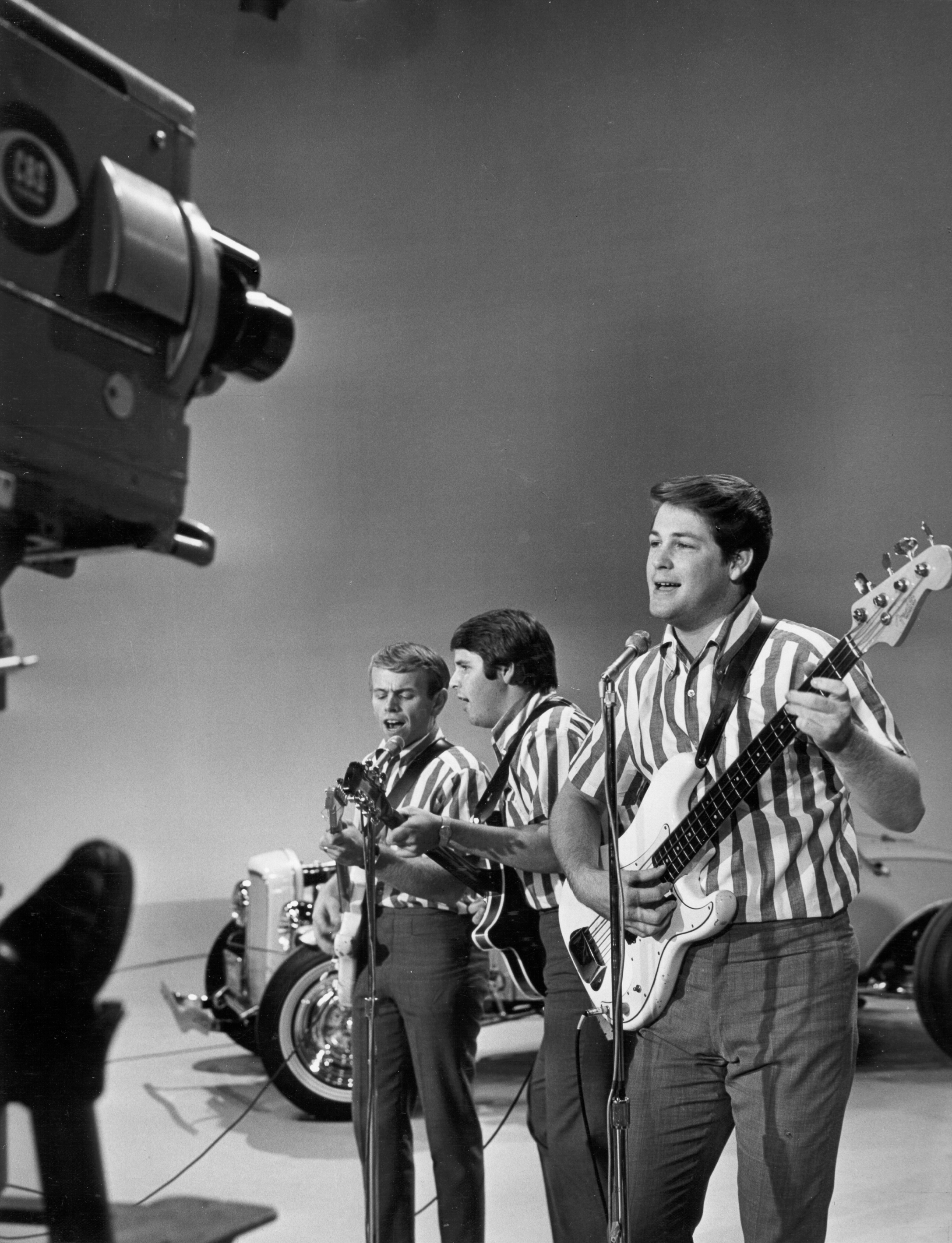 NEW YORK - SEPTEMBER 27: Al Jardine, Carl Wilson and Brian Wilson of the rock and roll band "The Beach Boys" perform the song "I Get Around" onstage on "The Ed Sullivan Show" in front of vintage hot rod cars on September 27, 1964 in New York City, New York. (Photo by Michael Ochs Archives/Getty Images)