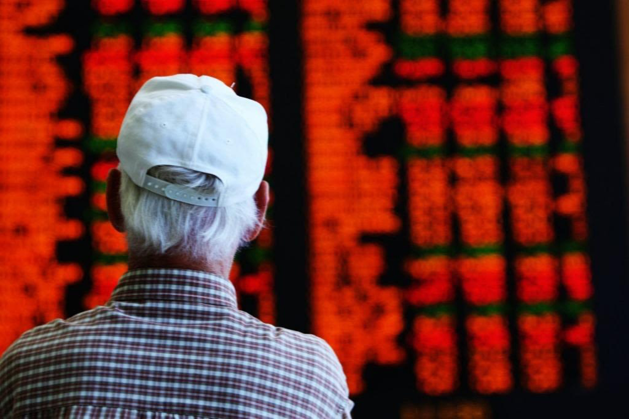 Un hombre mira un tablero del mercado de valores de ASX cubierto de números rojos.