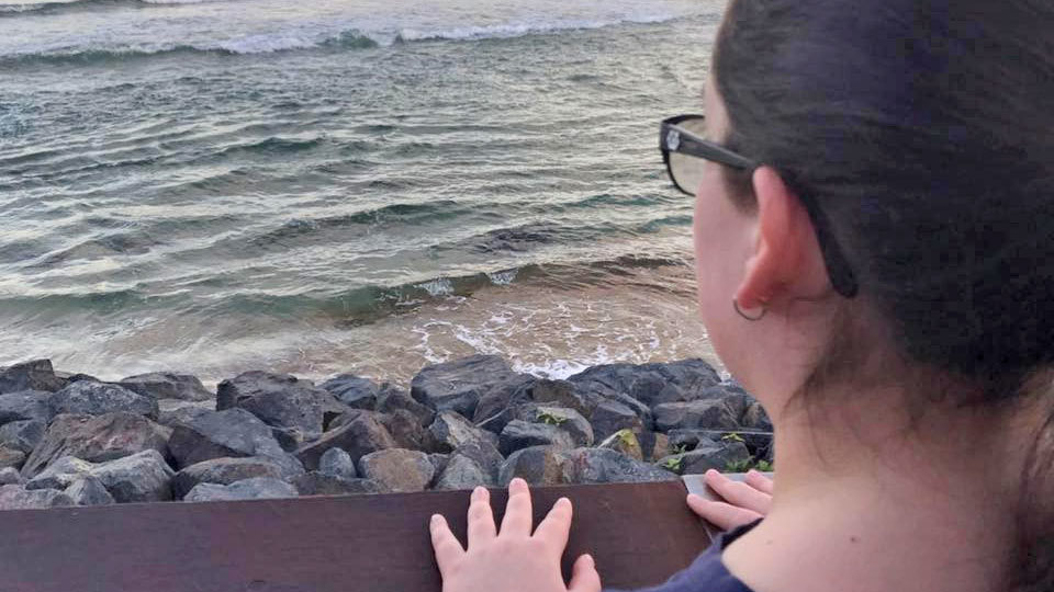 Tiana Offord stands with her hands placed on an ocean wall and looks out towards the sea.
