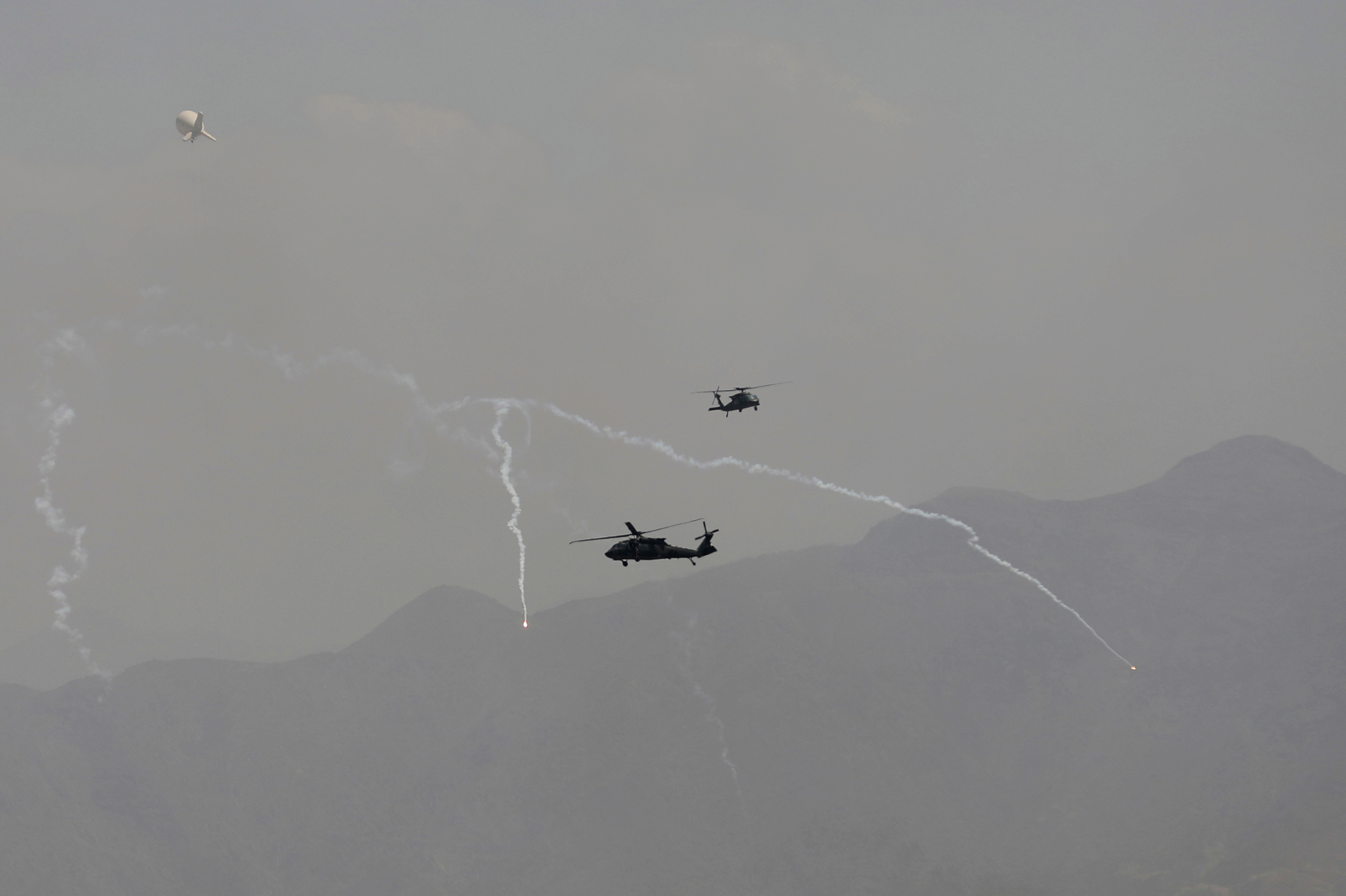 Anti-missile decoy flares are deployed as US Black Hawk military helicopters and a dirigible balloon fly over the city of Kabul.