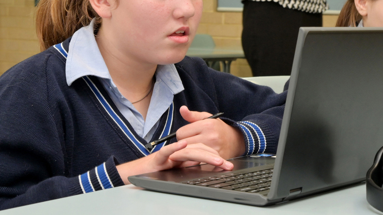 Technology teacher(Female  age 30-40) teaching schoolgirls how to use laptops in school classroom.