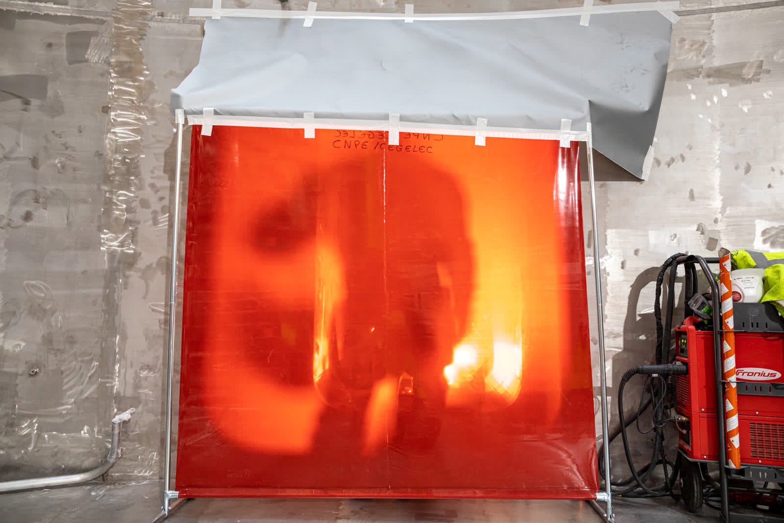 A welder stands behind a protective shield at the lowest level of the ITER cryostat base.