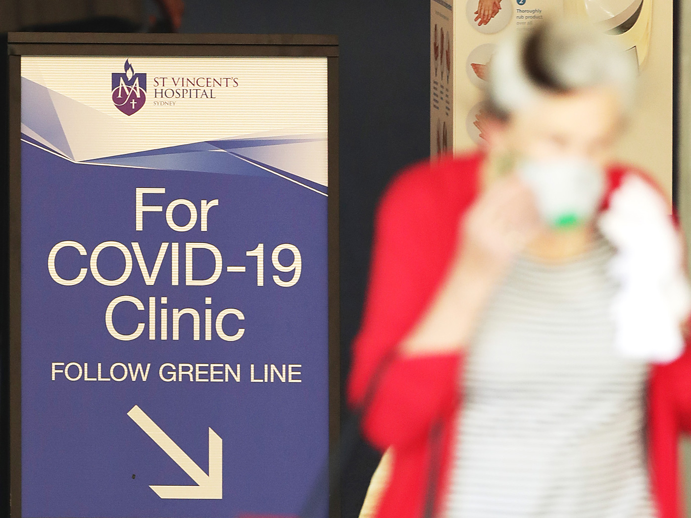 A woman passes a sign for a COVID -19 Clinic as she exits St Vincent's hospital in Sydney, Australia.