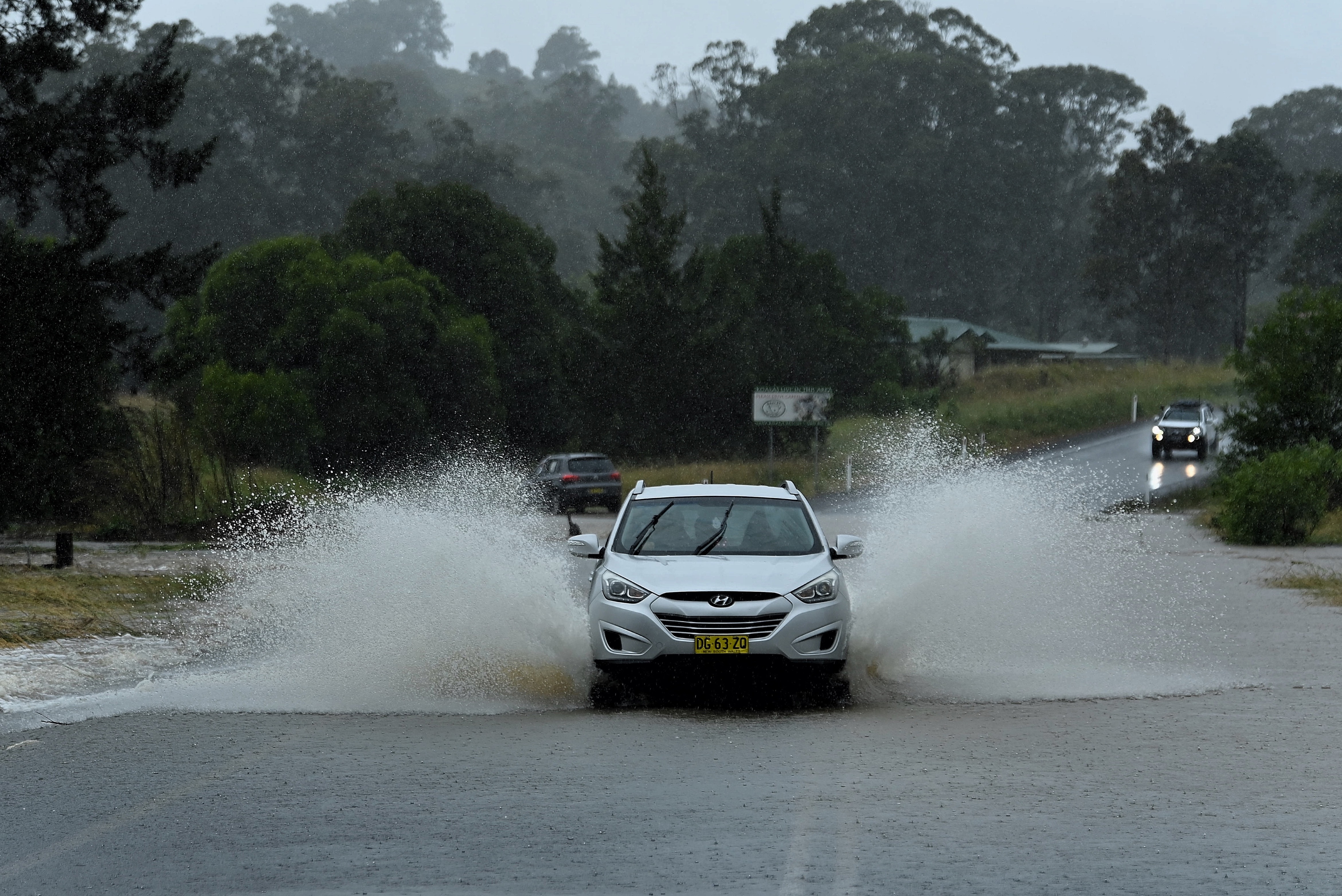 A vehicle drives through water on The Bucketts Way near Bo Bo Creek where water has flooded the road. 