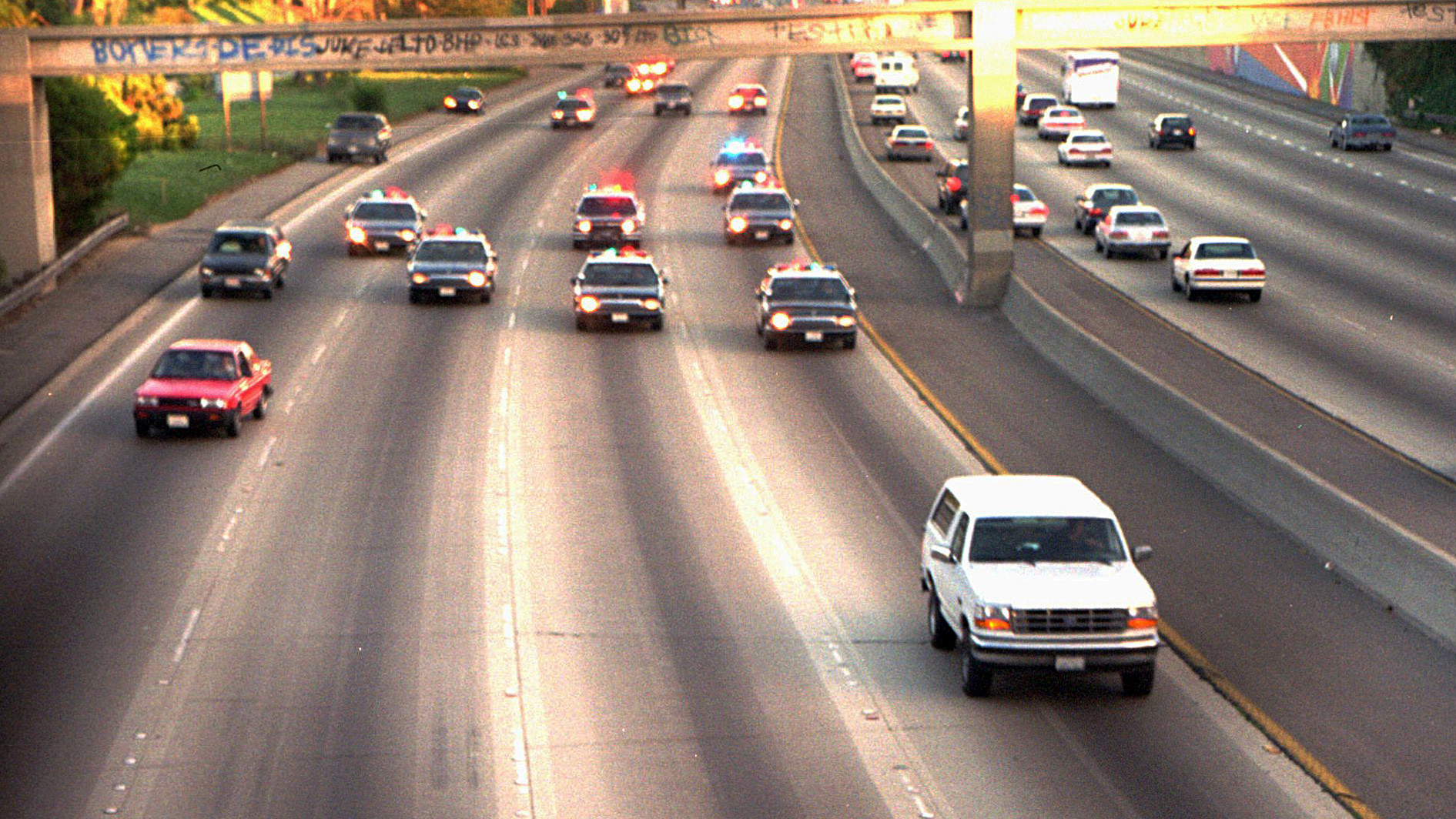 A white Ford Bronco, driven by Al Cowlings carrying O.J. Simpson, is trailed by Los Angeles police cars as it travels on a freeway in Los Angeles. Simpson's ex-wife, Nicole Brown Simpson, and her friend Ronald Goldman had been found dead in Los Angeles, four days earlier. Simpson is later arrested after a widely televised freeway chase in his white Ford Bronco.