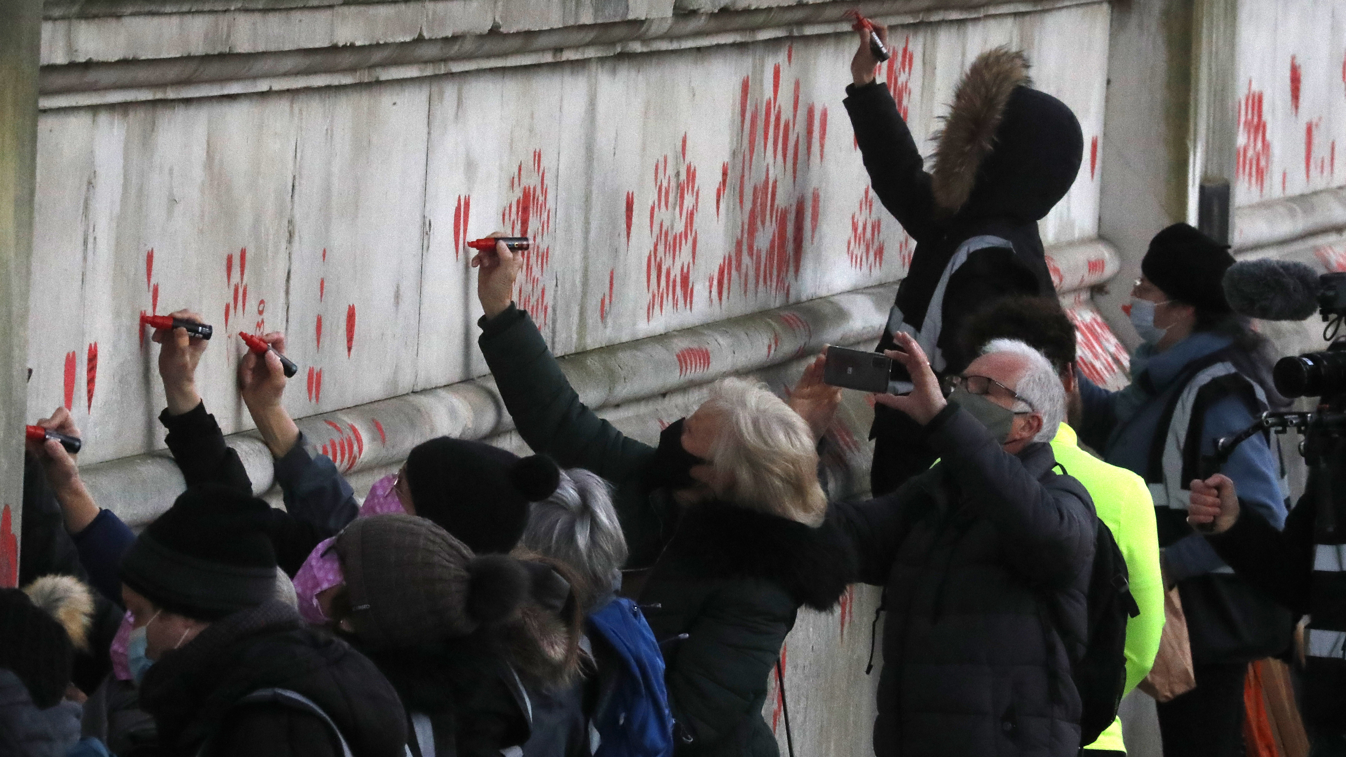 People paint red hearts onto the COVID-19 Memorial Wall mourning those who have died, opposite the Houses of Parliament on the Embankment in London.