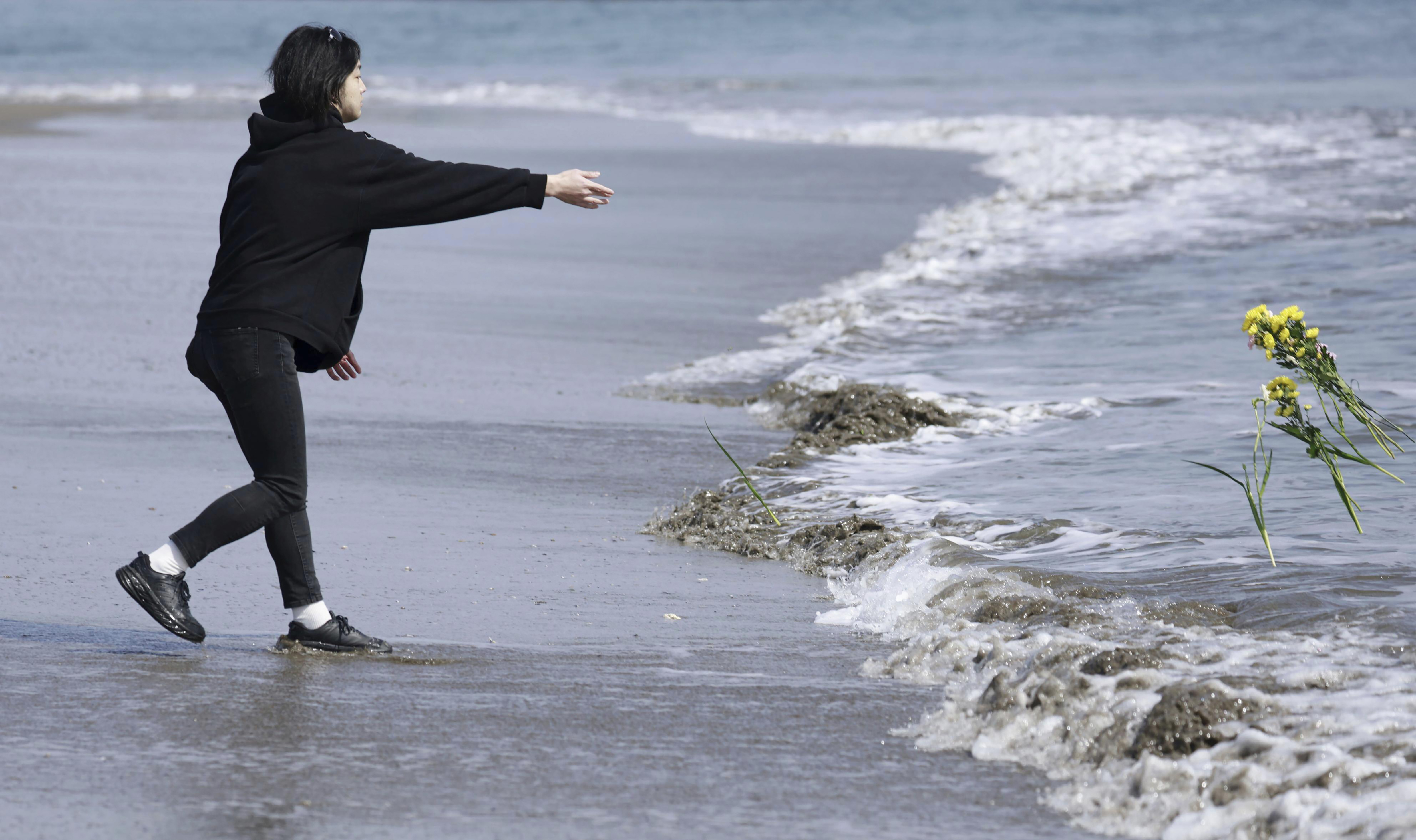 A man throws flower to the sea in tribute to the victims in the 2011 earthquake and tsunami in Arahama area, Sendai city, northern Japan, on Saturday, March 11, 2023.