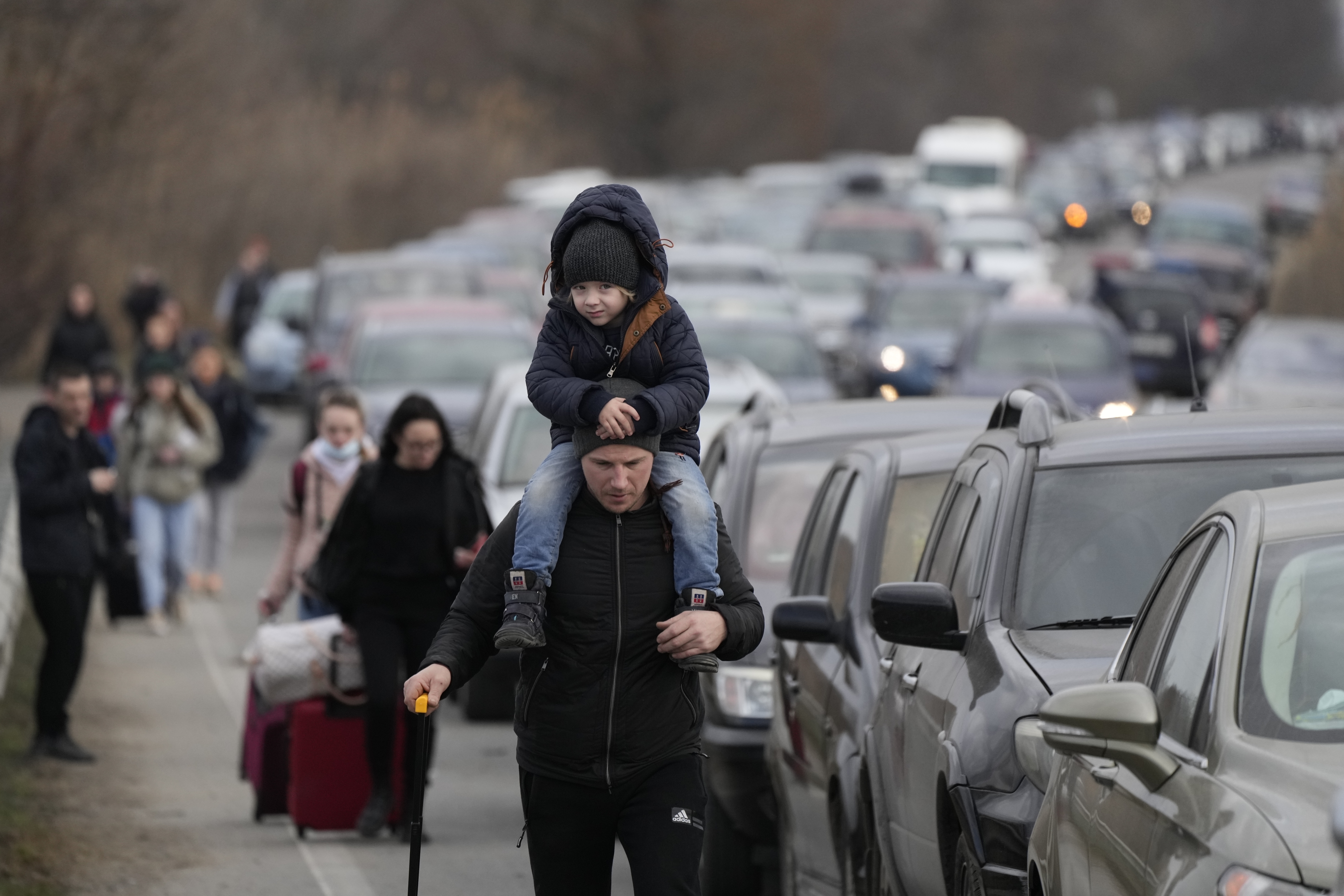 Ukrainian refugees walk along vehicles lining-up to cross the border from Ukraine into Moldova, at Mayaky-Udobne crossing border point near Mayaky-Udobne, Ukraine, Saturday, Feb. 26, 2022. The U.N. refugee agency says nearly 120,000 people have so far fled Ukraine into neighboring countries in the wake of the Russian invasion. The number was going up fast as Ukrainians grabbed their belongings and rushed to escape from a deadly Russian onslaught. (AP Photo/Sergei Grits)