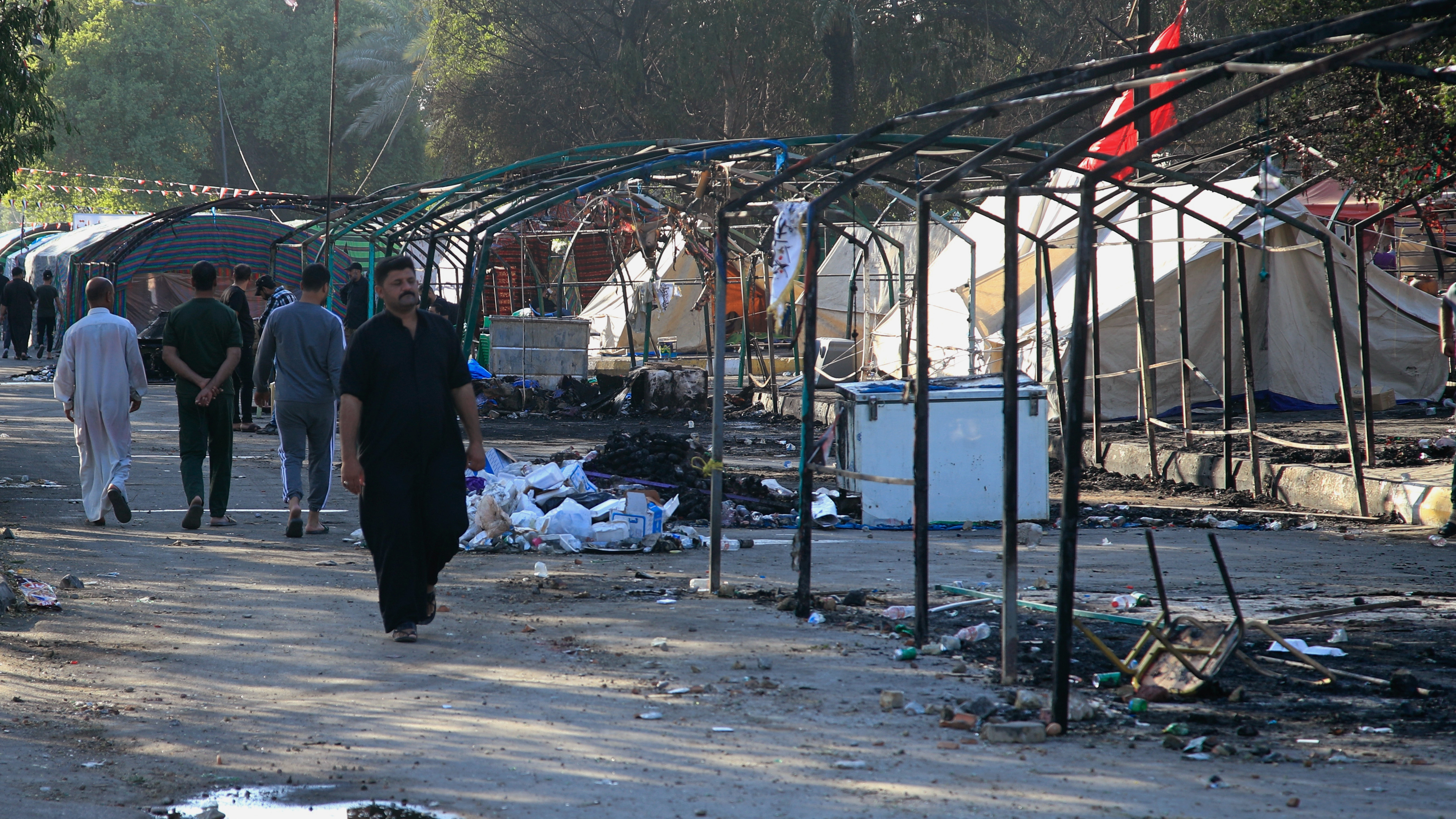 People walk amid burned tents outside the heavily fortified Green Zone in Baghdad, Iraq.