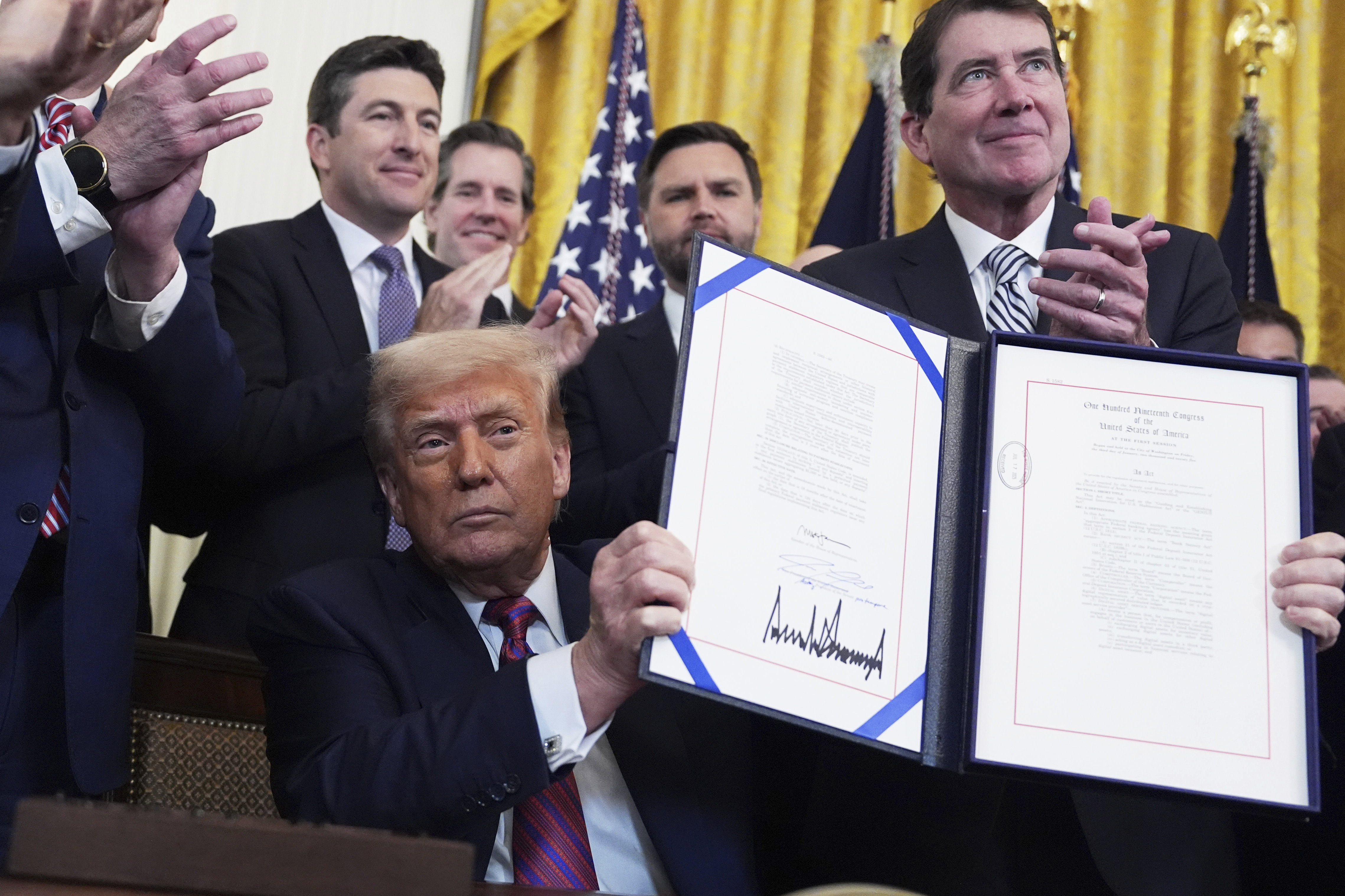 President Donald Trump holds up the signed document after signing the GENIUS Act