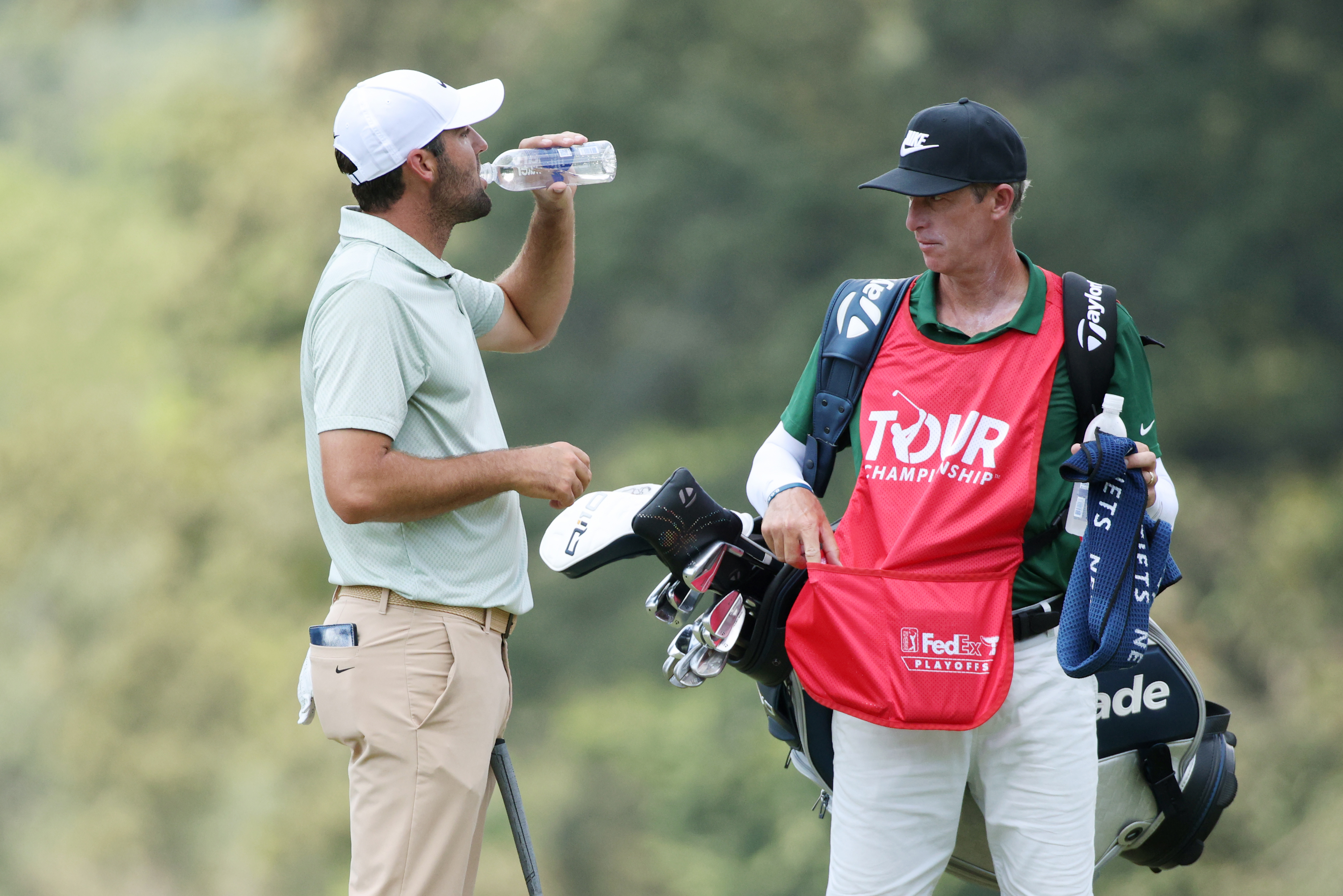 Scottie Scheffler of the United States takes a drink on the second green as his caddie Ted Scott looks on during the final round of the TOUR Championship at East Lake Golf Club on September 01, 2024 in Atlanta, Georgia. (Photo by Mike Mulholland/Getty Images)