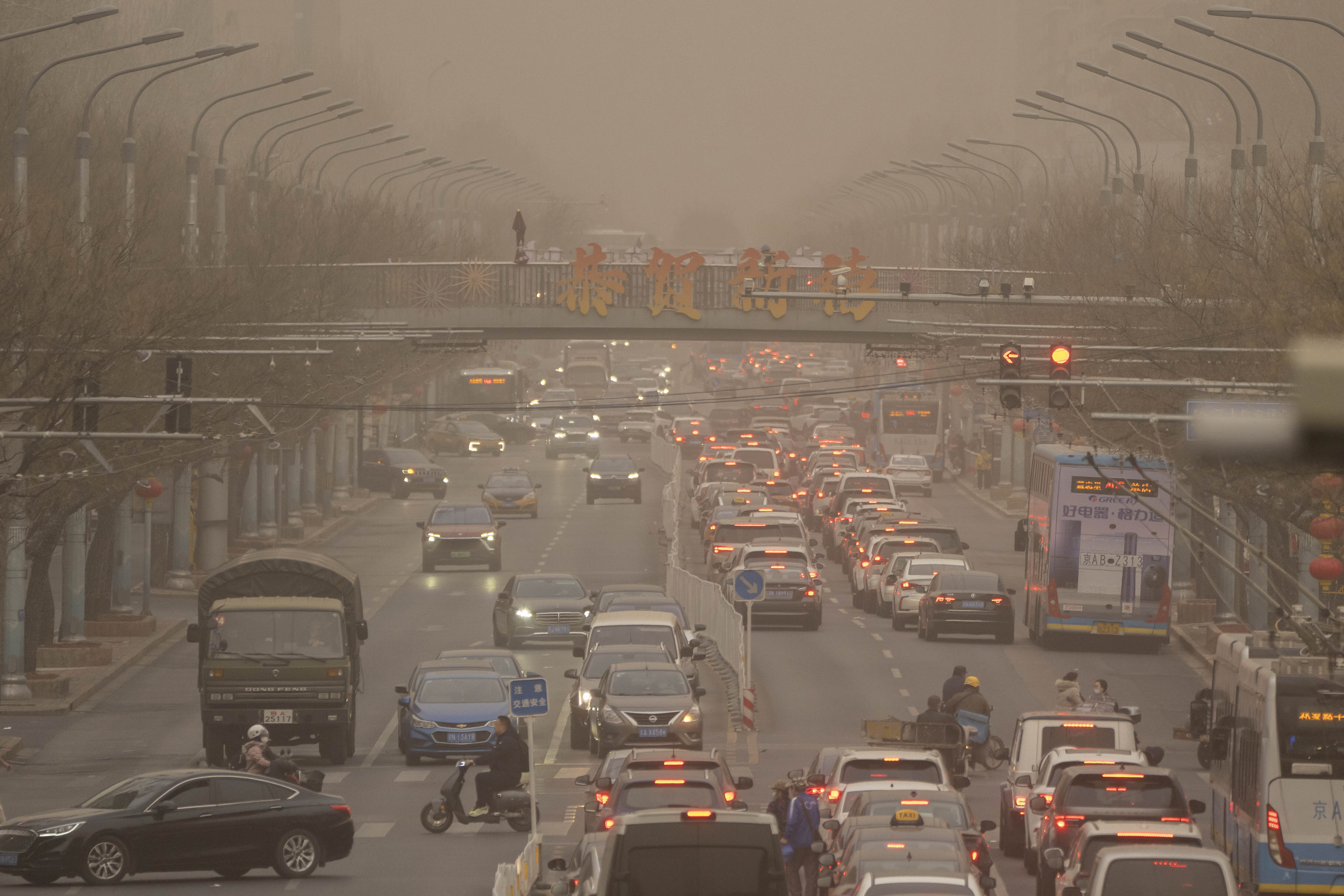 Cars and pedestrians navigate along a street shrouded in dust and haze in Beijing, Friday, March 10, 2023. 