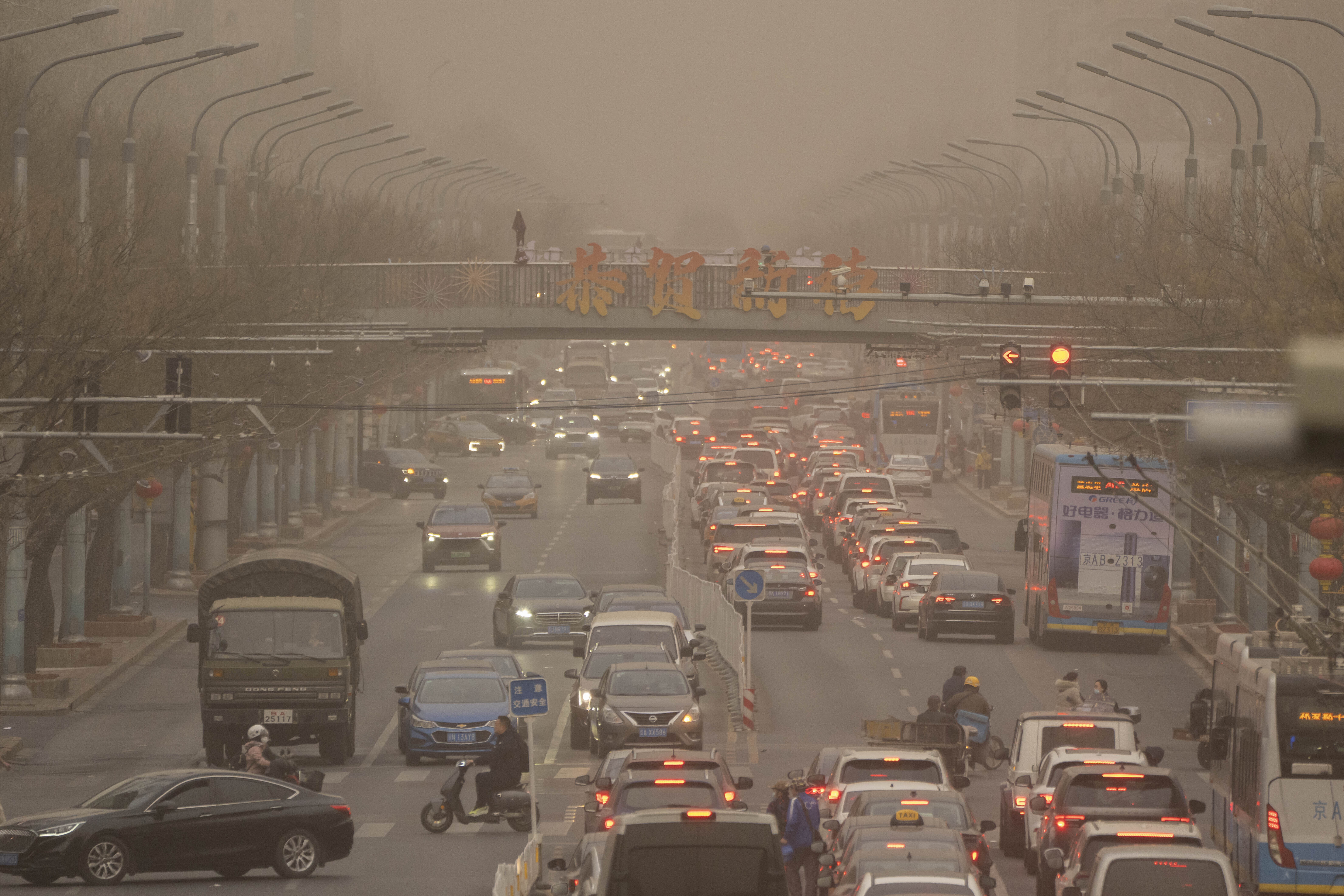 Cars and pedestrians navigate along a street shrouded in dust and haze in Beijing, Friday, March 10, 2023.