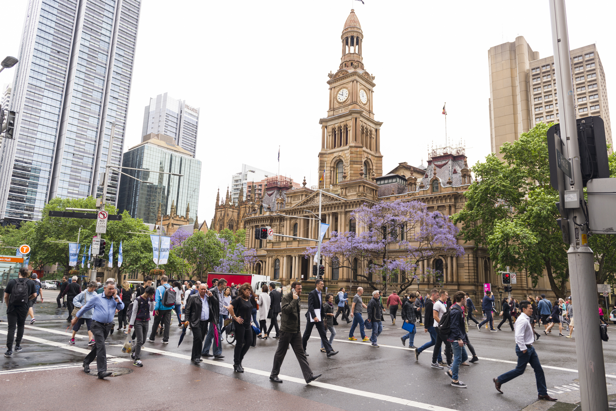 Sydney Town Hall is Victorian style sandstone building, built in the 1880. A prominent landmark building and popular meeting place. Sydney, Australia - November 5, 2015: People are crossing the junction of George Street and Park Street. Sydney Town Hall is in the background.