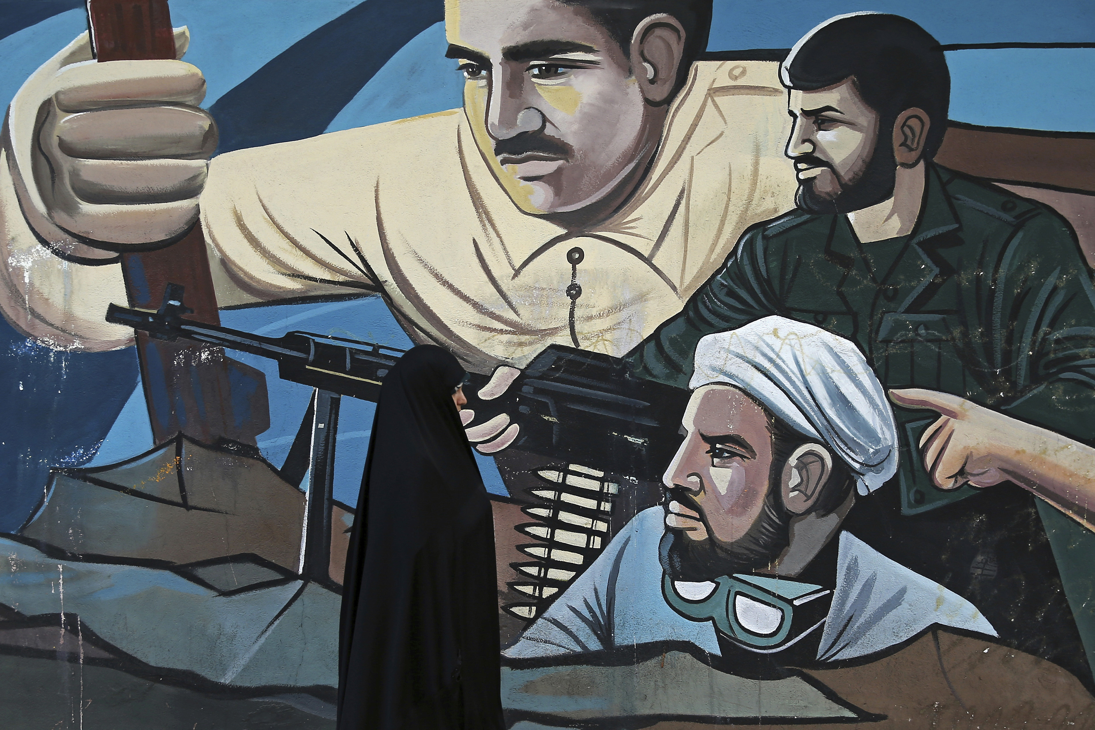 An Iranian woman walks on a sidewalk in front of graffiti depicting members of Iranian Basij paramilitary force , in downtown Tehran, Iran, Wednesday, Jan. 3, 2018.