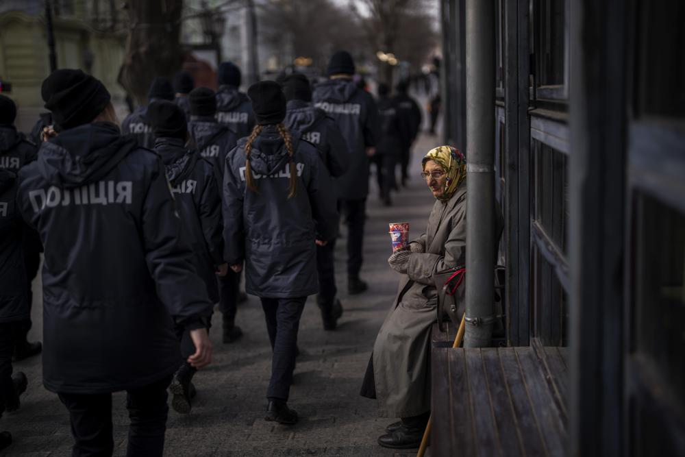 Ukrainian police officers march past a woman begging for alms during a demonstration in Odessa, Ukraine. 