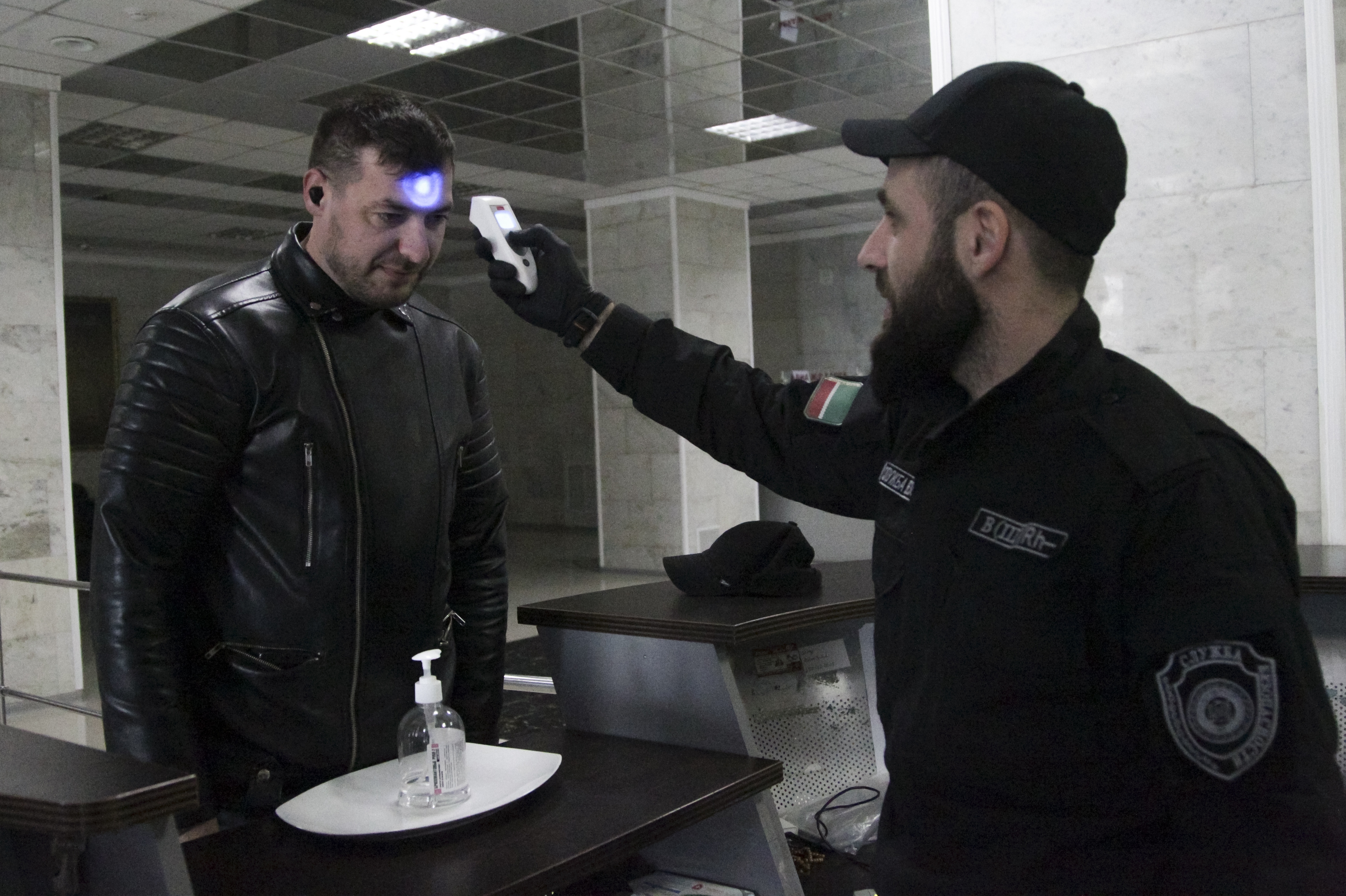 An security checks the body temperature of a man at an entrance of a building in Chechen provide capital Grozny, Russia.
