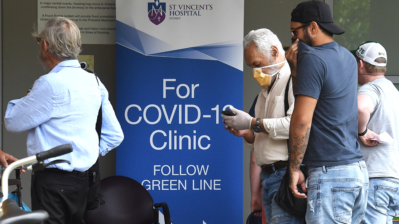 People wearing face masks walk past the sign for the COVID-19 Clinic at St Vincent's Hospital in Darlinghurst, Sydney. 