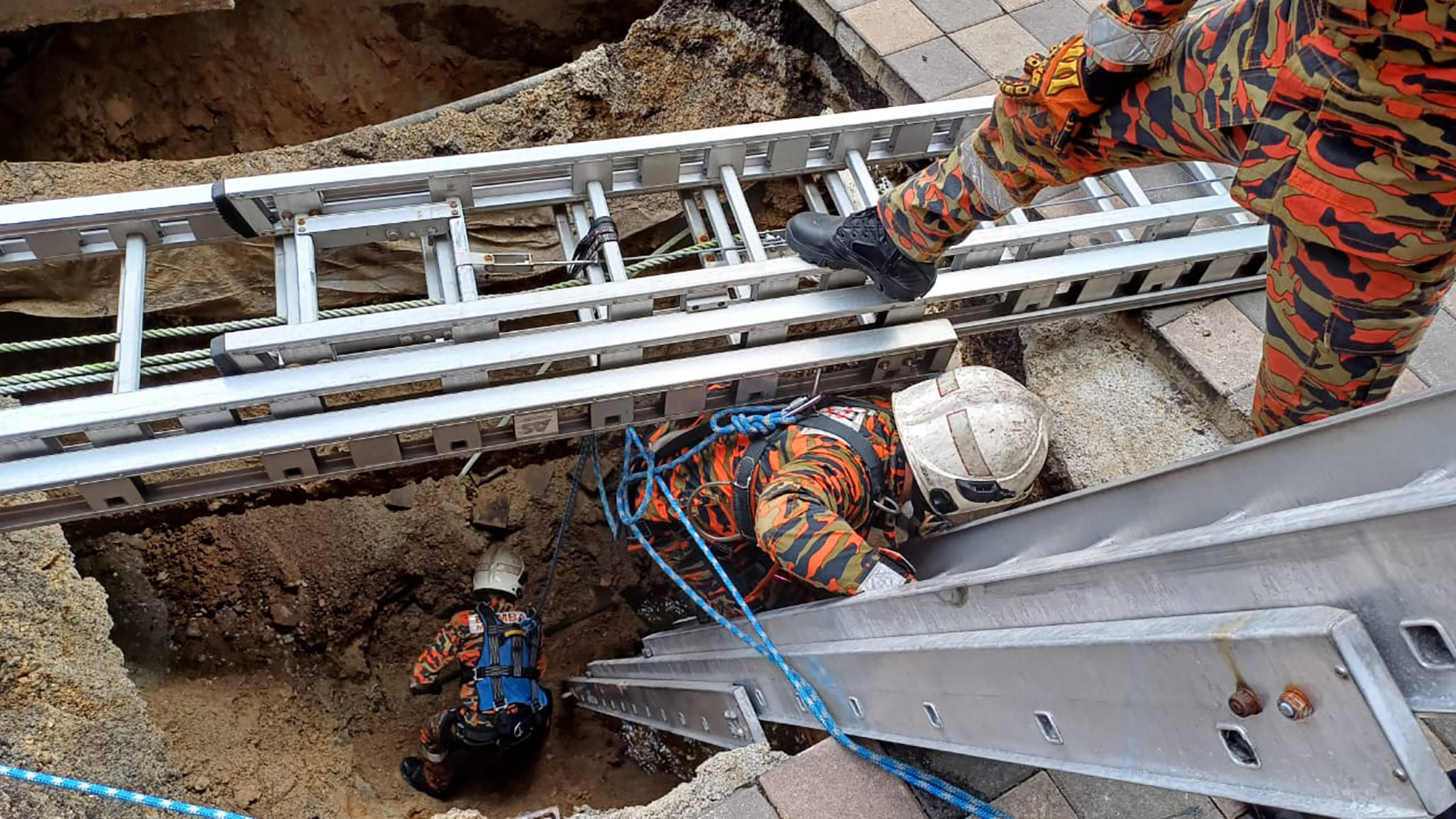 This photograph provided by Fire and Rescue Department of Malaysia, shows rescue personnel entering a deep sinkhole after receiving reports that a woman has fallen into the sinkhole after a section of the sidewalk caved in Kuala Lumpur, Friday, Aug. 23, 2024 