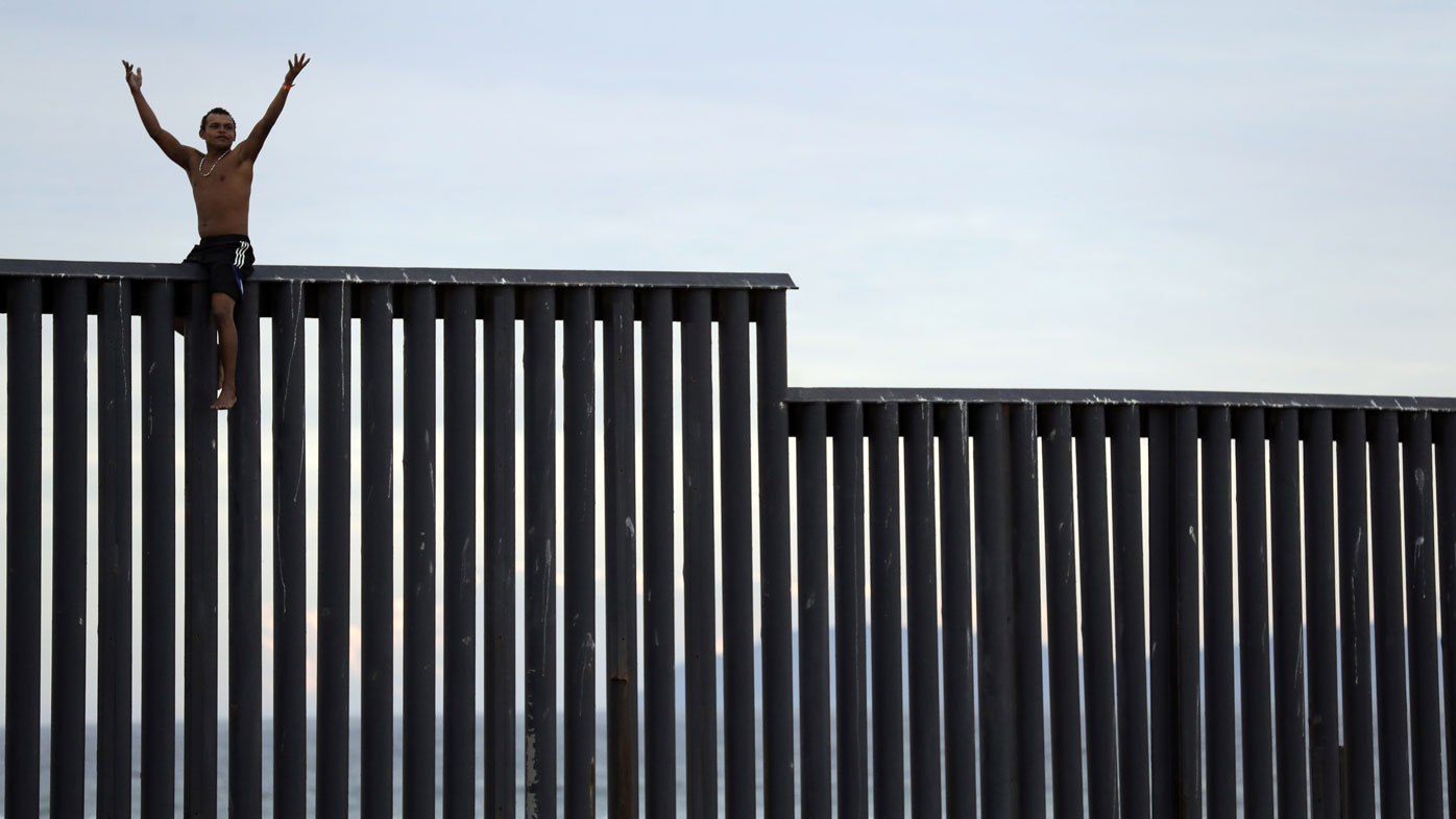 A member of the migrant caravan sits atop the border wall between the United States and Mexico.