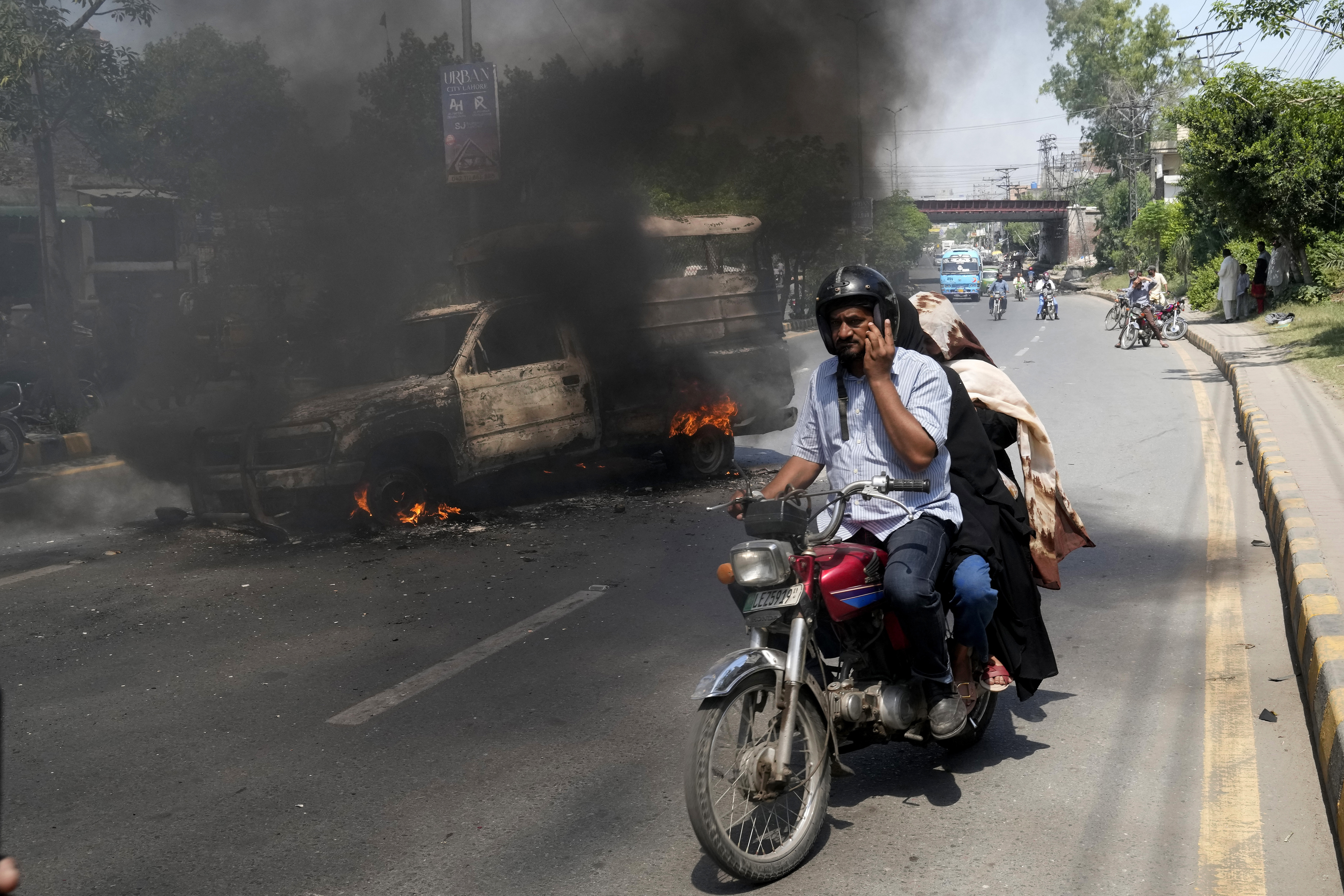 A motorcyclist drives past a burning vehicle set on fire by angry supporters of Pakistan's former Prime Minister Imran Khan, in Lahore, Pakistan, Thursday, May 11, 2023.  
