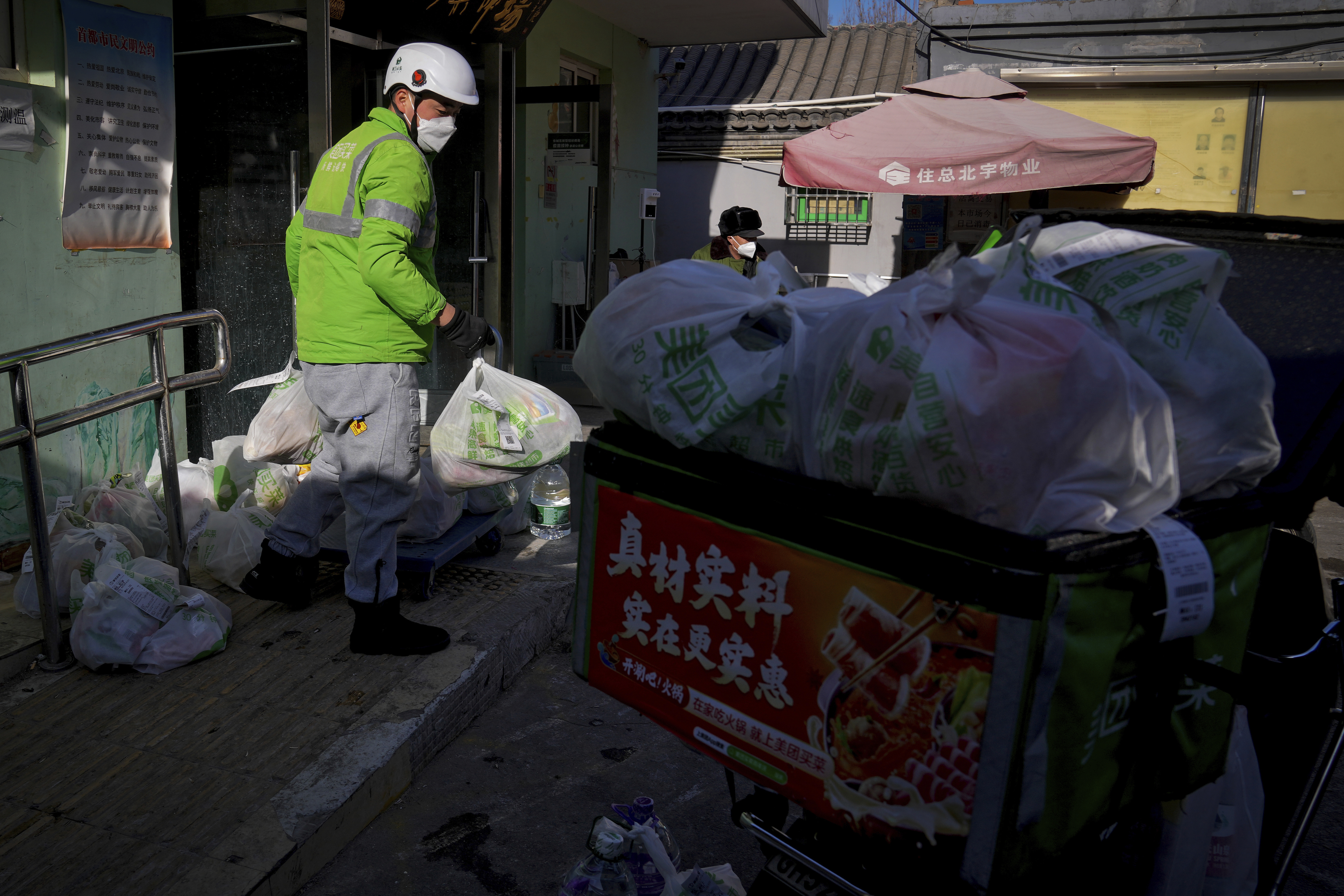 A delivery rider collects bags of online grocery orders as a surge of COVID-19 cases is causing a shortage of delivery workers in Beijing, Sunday, Dec. 18, 2022. (AP Photo/Andy Wong)