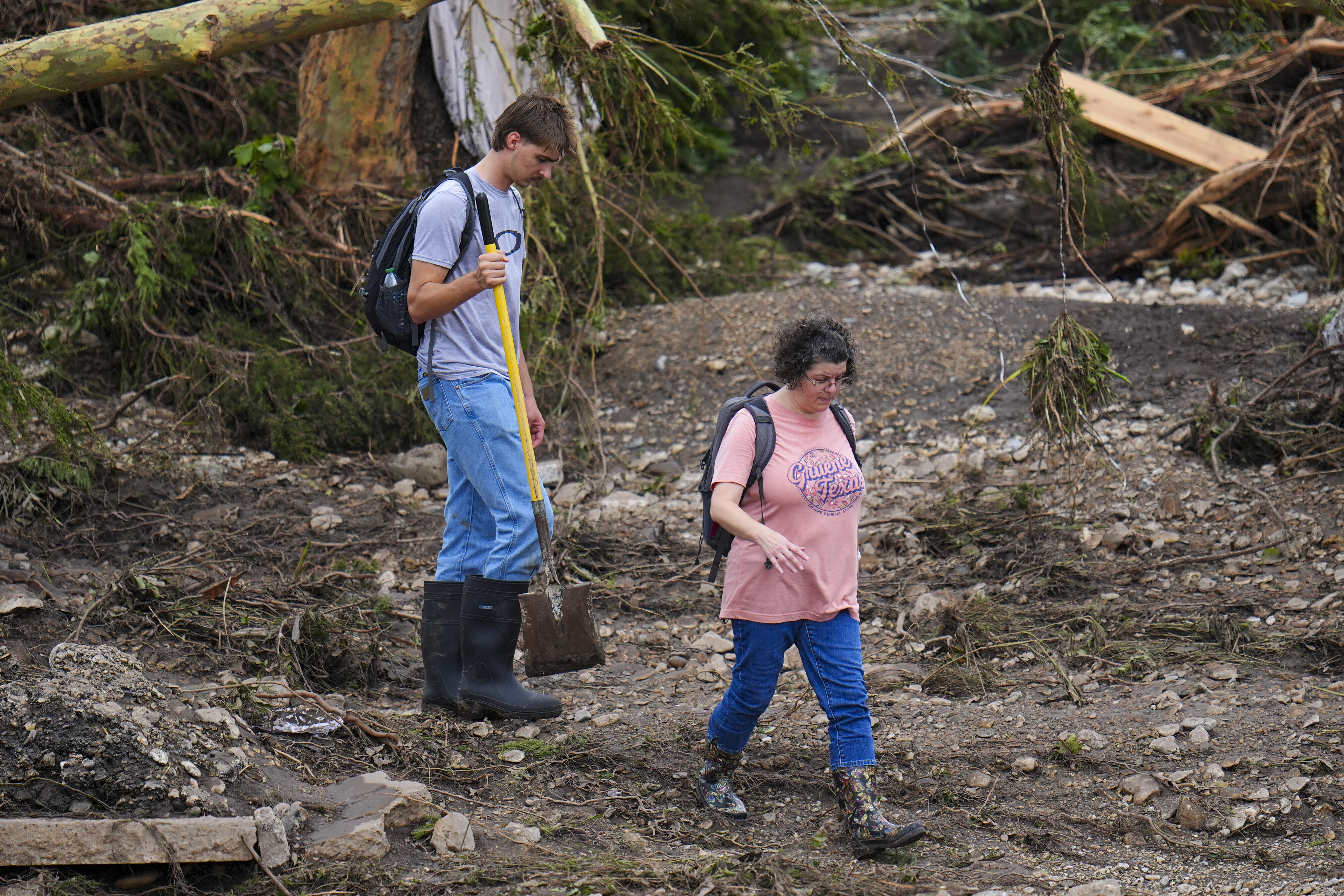 People walk along debris near the banks of the Guadalupe River after a flash flood swept through the area Saturday, July 5, 2025, in Hunt, Texas. (AP Photo/Julio Cortez)