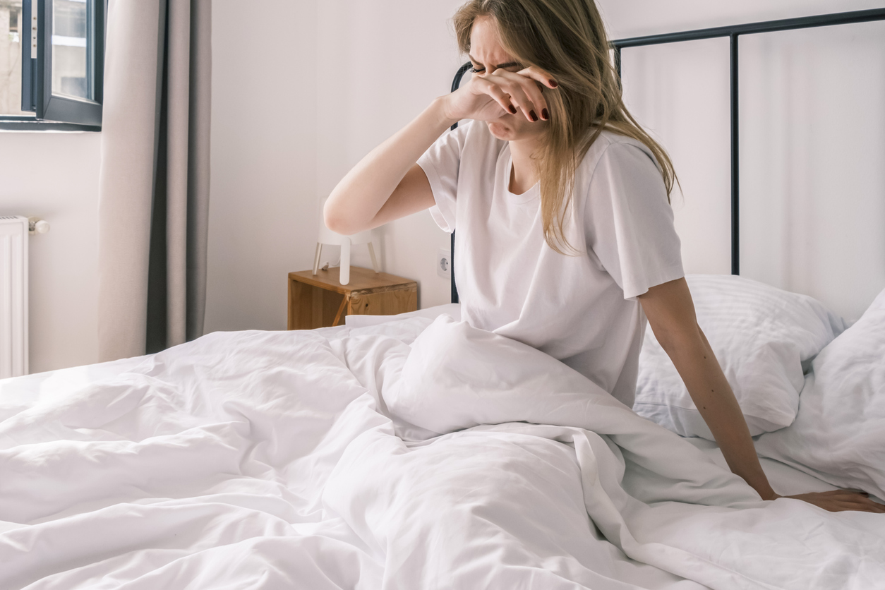 Sleepy young woman rubs her eyes while sitting in bed in the morning feeling tired after waking up. Bad restless sleep. stress, nightmares